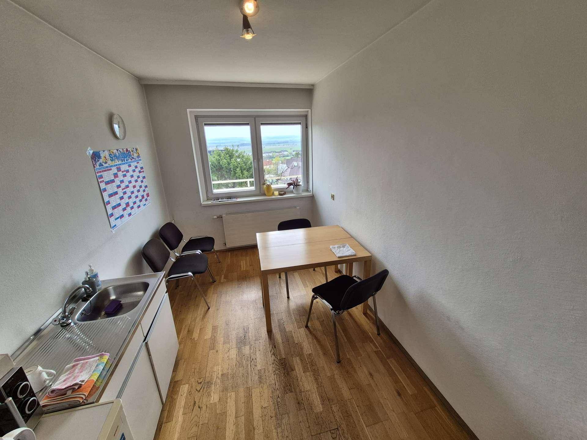 Kompakte Teeküche mit Holzboden, Spüle, Kühlschrank und einem kleinen Esstisch.