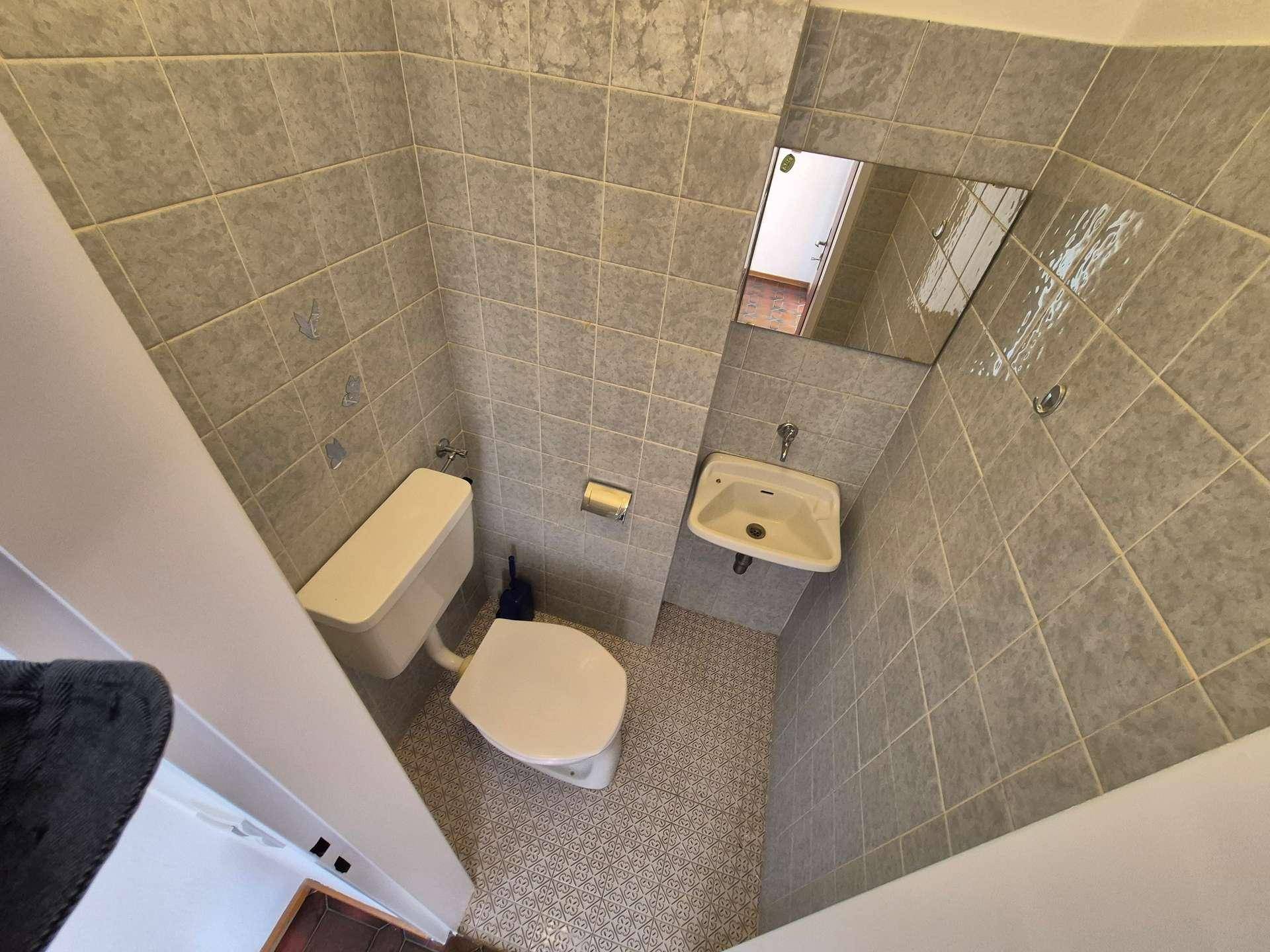 Kleines Gäste-WC mit grauen Fliesen, Toilette und Handwaschbecken, praktisch und kompakt.
