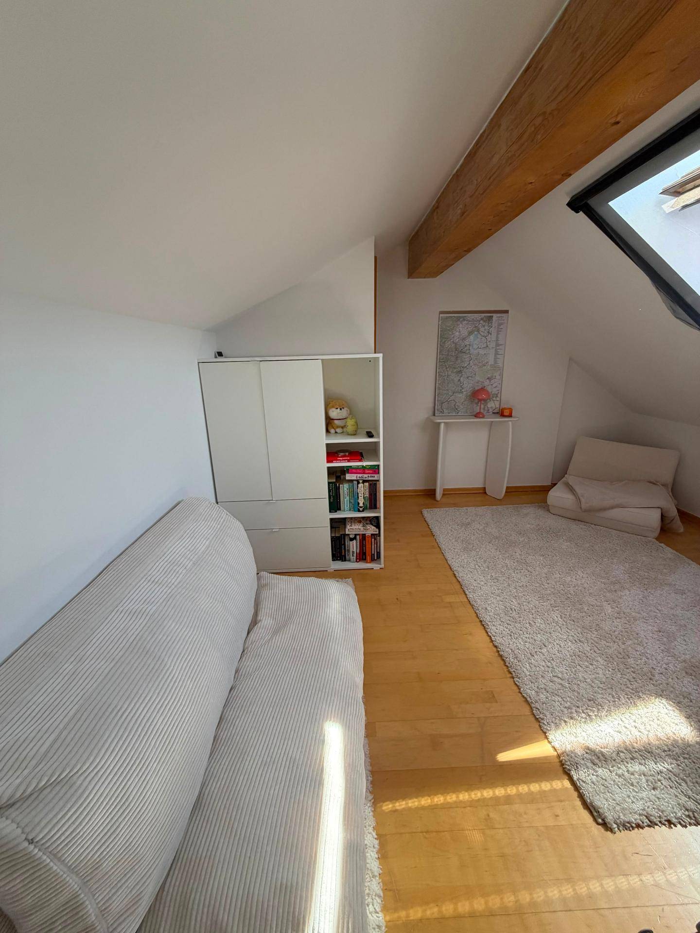 Helles Zimmer im Dachgeschoss mit Dachschräge, Holzbalken und Sofa.