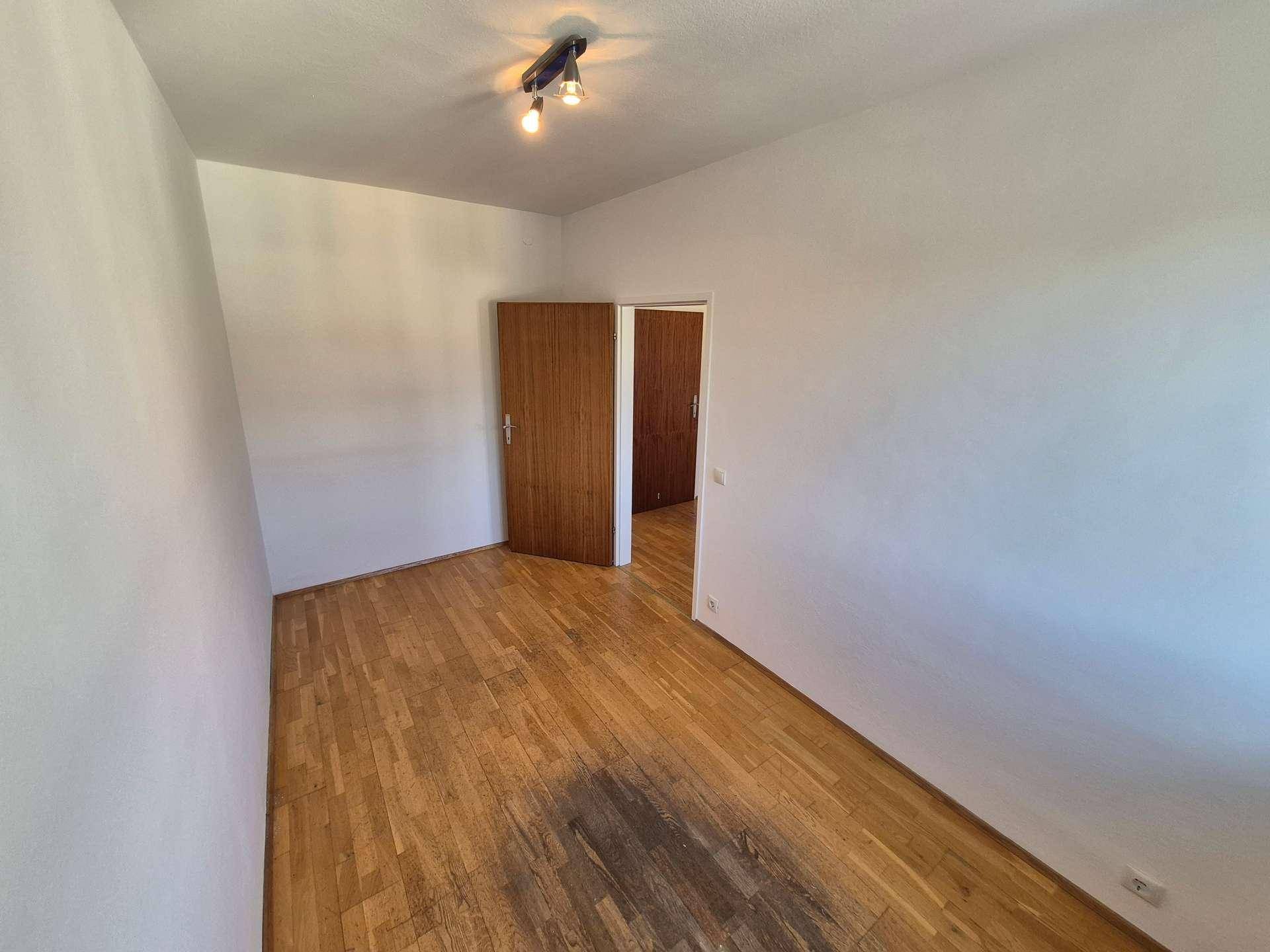Leeres Schlafzimmer mit Holzboden und einer Tür, die den Zugang zu weiteren Räumen ermöglicht.