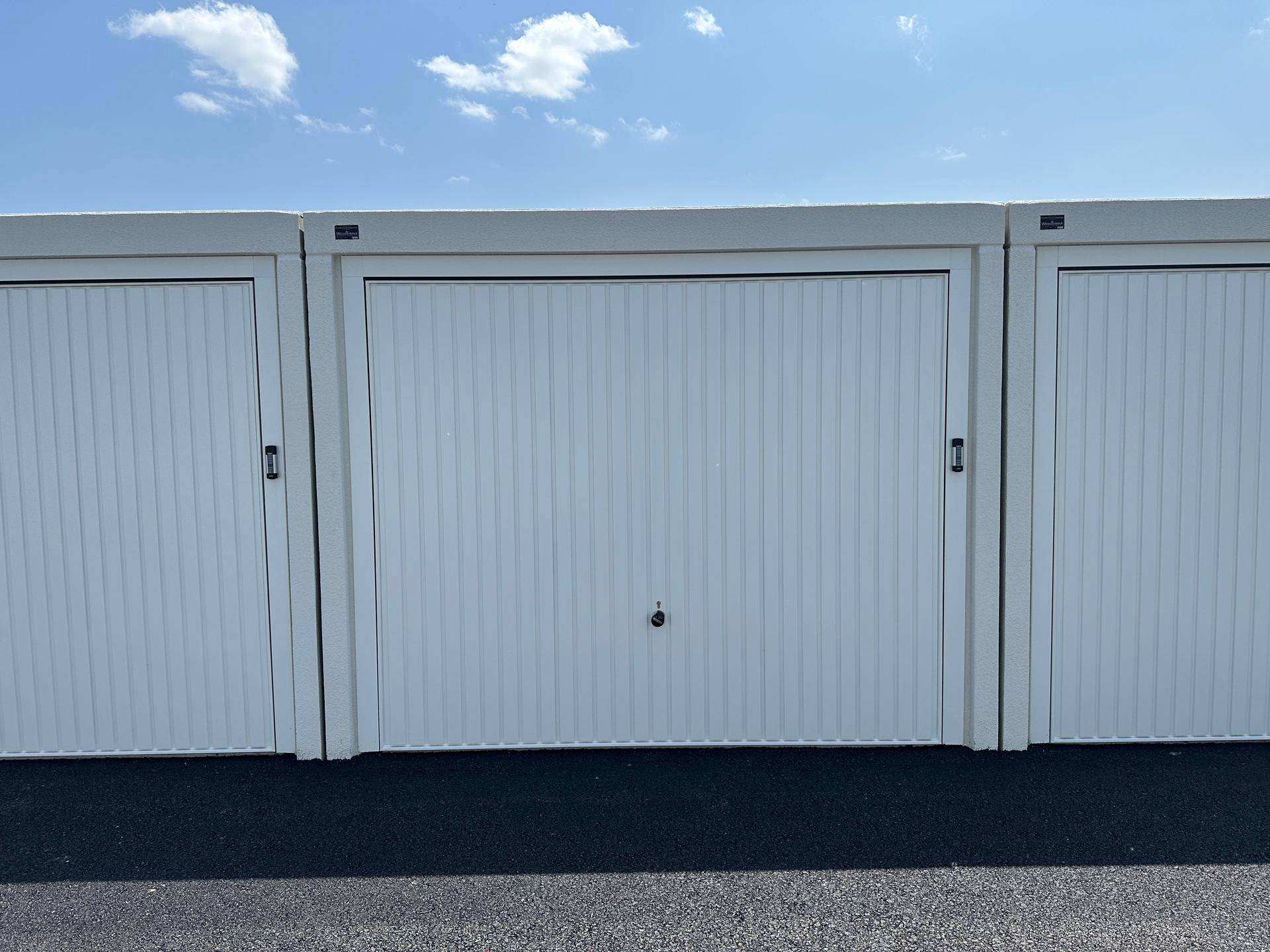 Nahaufnahme von drei identischen weißen Garagentoren mit vertikalen Lamellen und schwarzen Griffen.