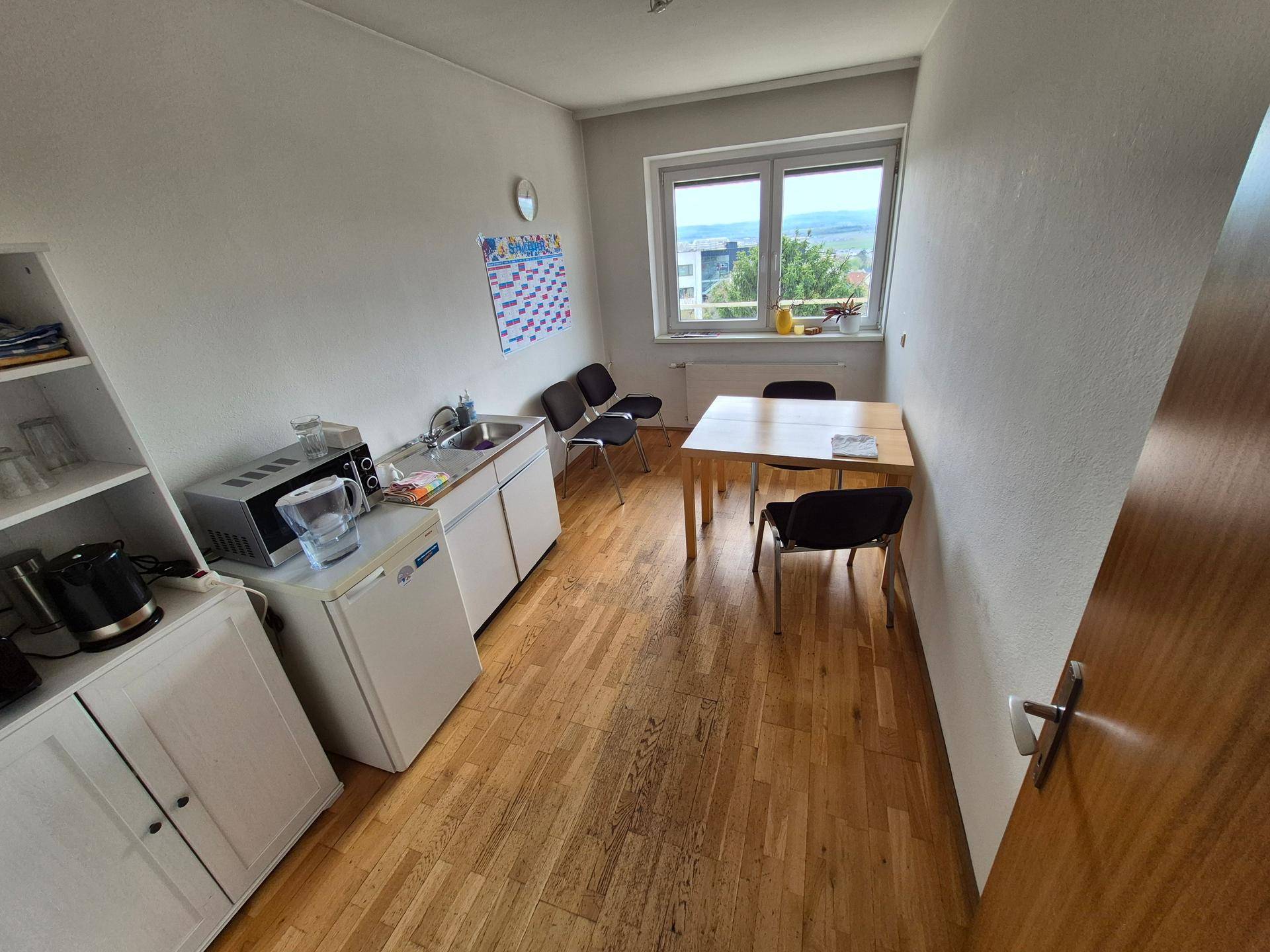 Kleine Teeküche mit Spüle, Kühlschrank, Mikrowelle und einem Esstisch am Fenster.