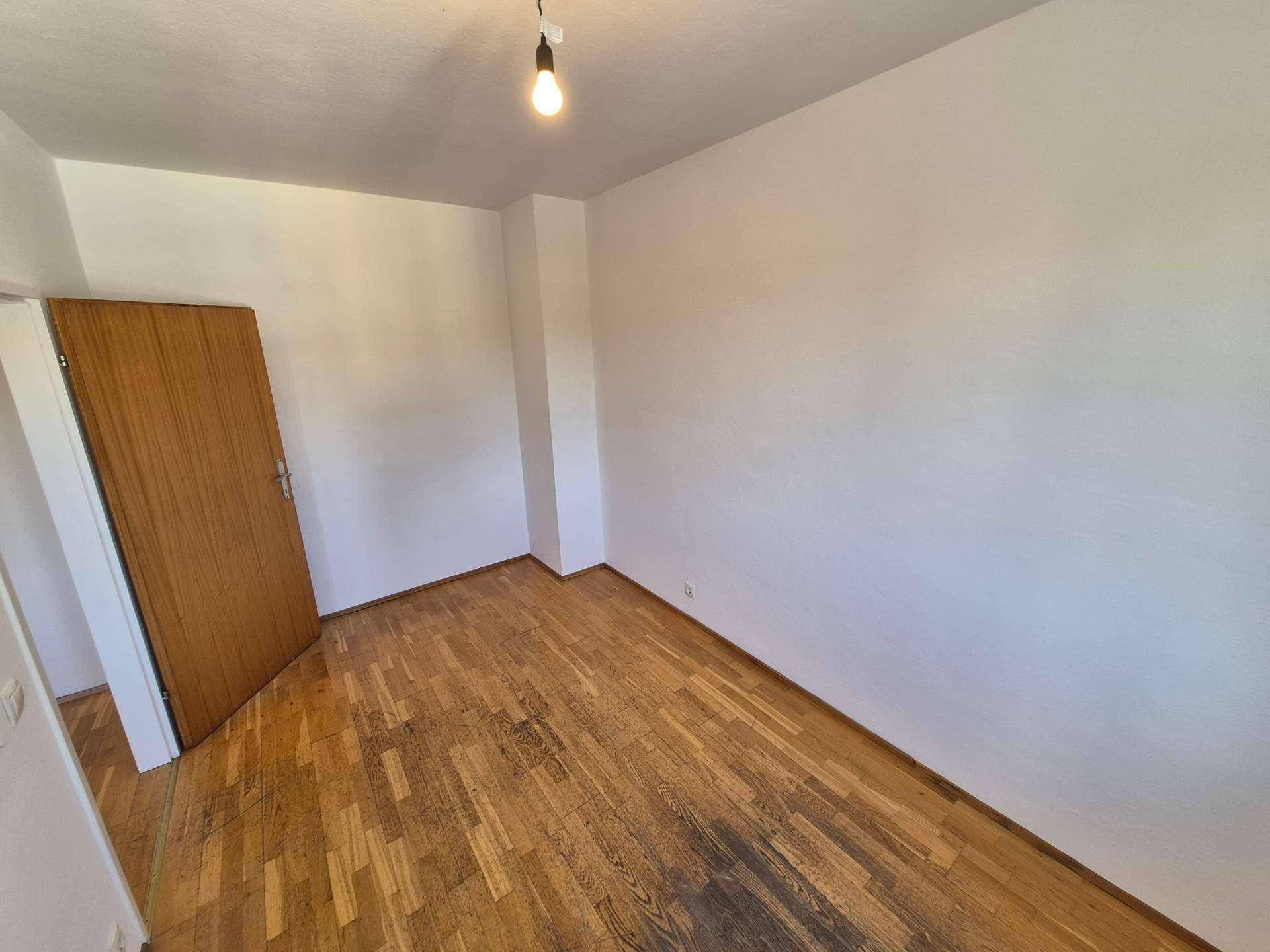 Einfaches Schlafzimmer mit Holzboden und weiß gestrichenen Wänden, bereit zur individuellen Gestaltung.