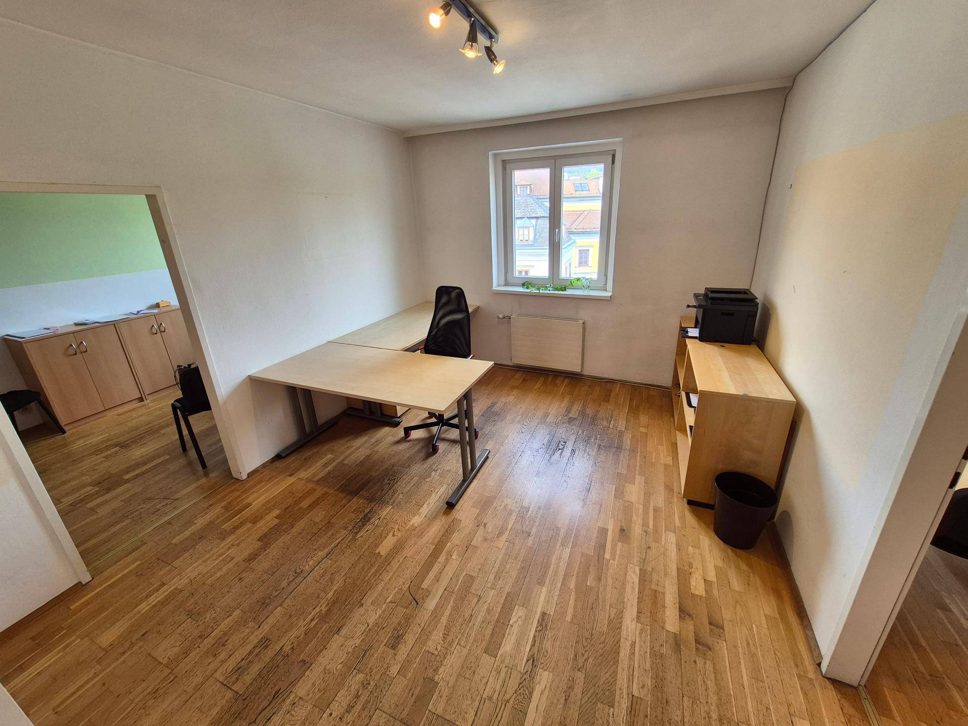 Großes Büro mit Holzboden, mehreren Schreibtischen und einem Drucker auf einem Regal.
