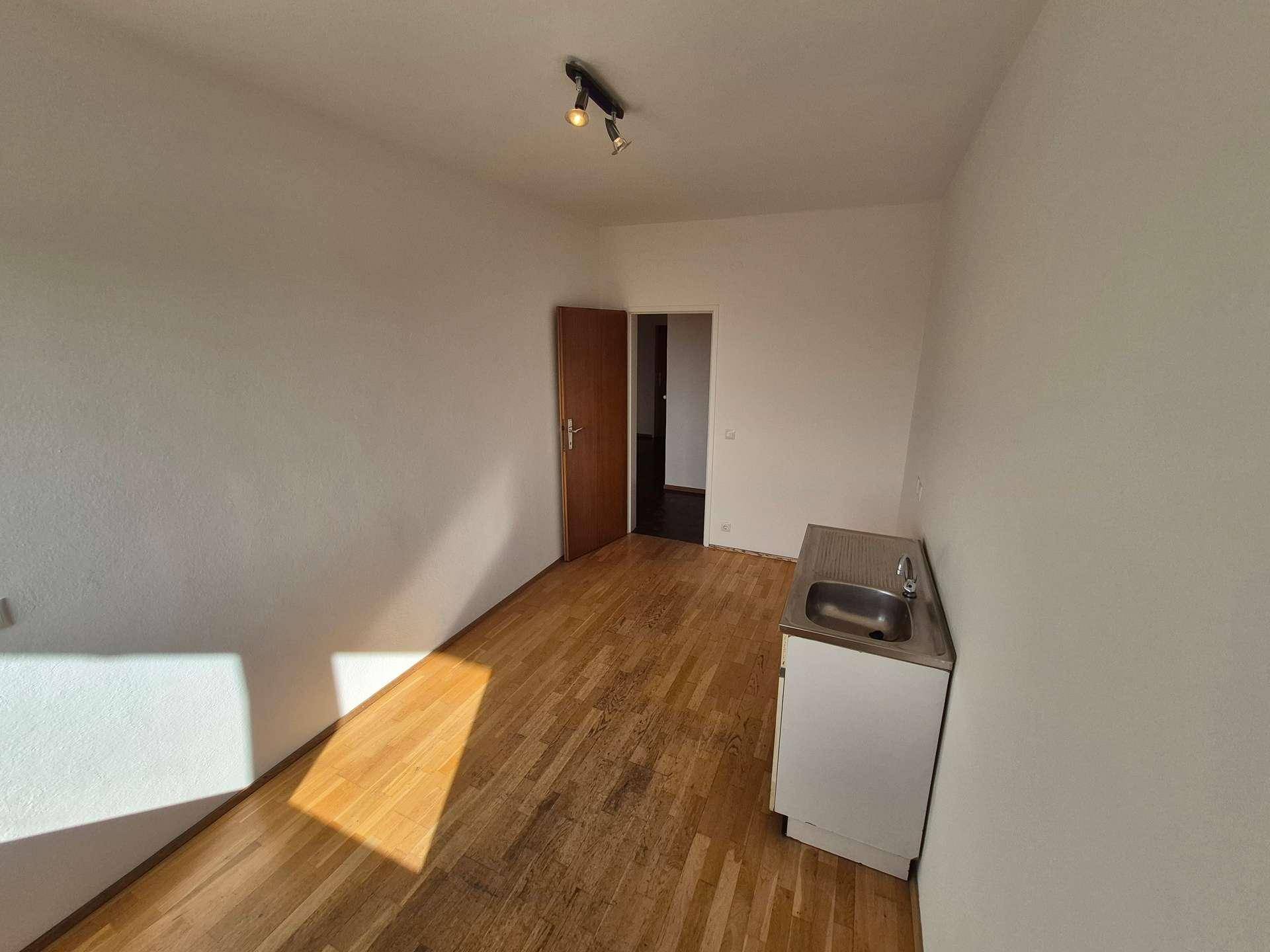 Raum mit Holzboden und einer einfachen Küchenzeile, die vielseitig genutzt werden kann.