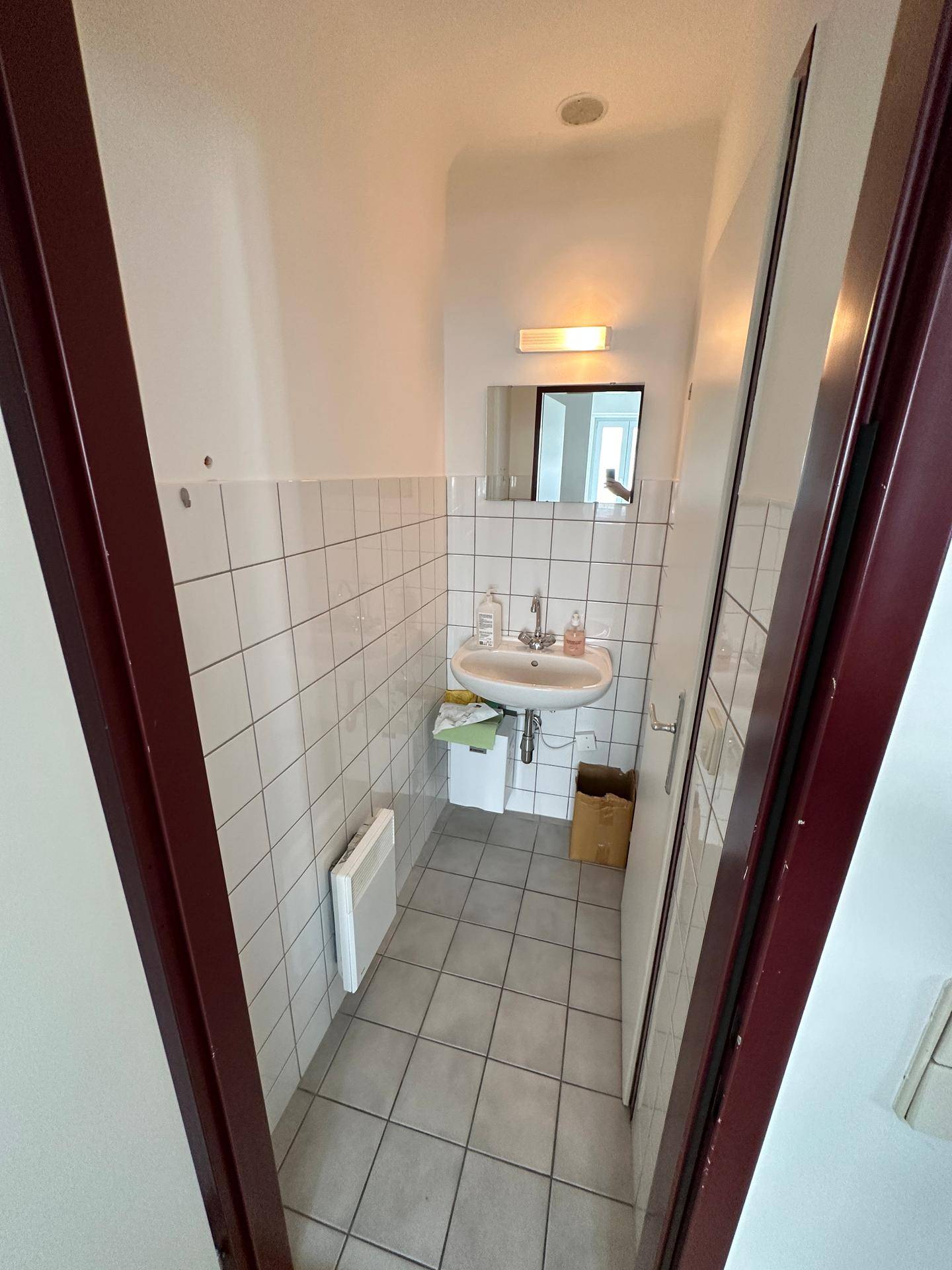 Kleines, gefliestes Gäste-WC mit Waschbecken und Spiegel, funktional und sauber.