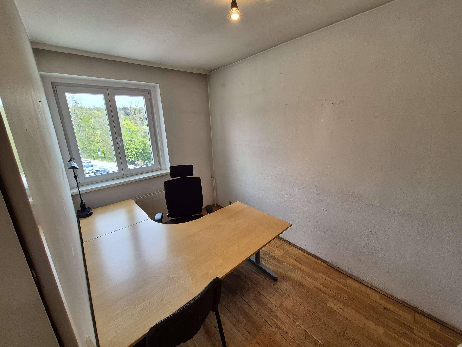 Helles Büro mit Holzboden, großem Schreibtisch und Fenster mit Blick ins Grüne.