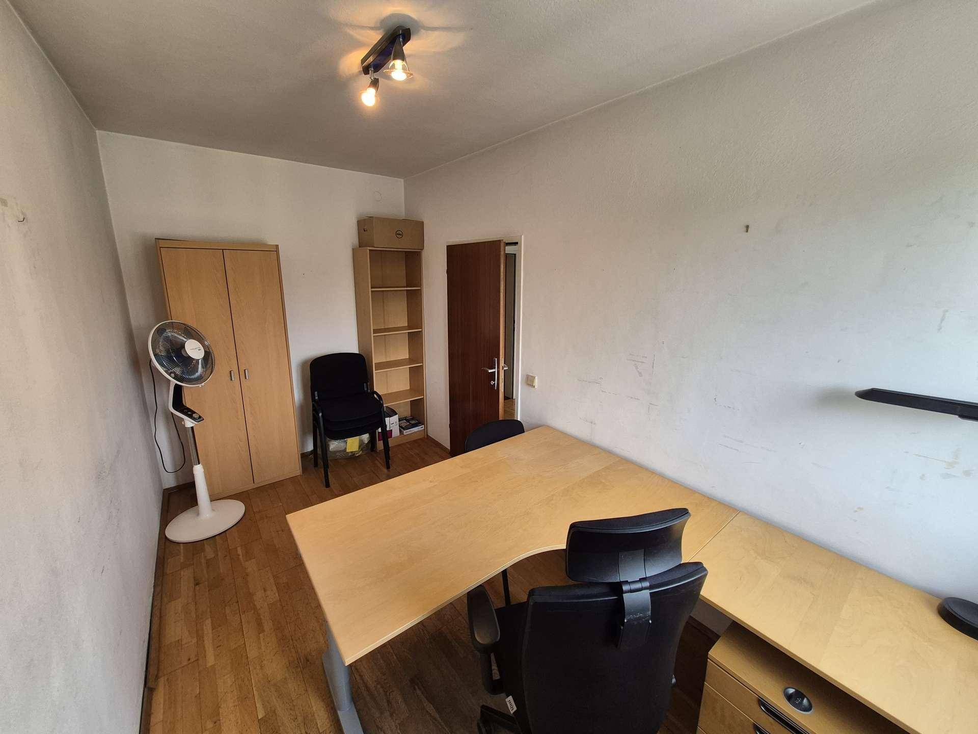 Büro mit Holzboden, großem Schreibtisch, Schrank und einem Ventilator für angenehmes Klima.