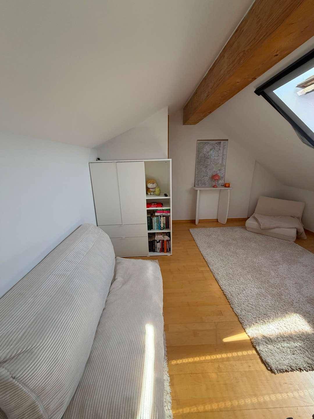 Dachgeschosszimmer mit sichtbarem Holzbalken, Dachfenster und schrägen Wänden.