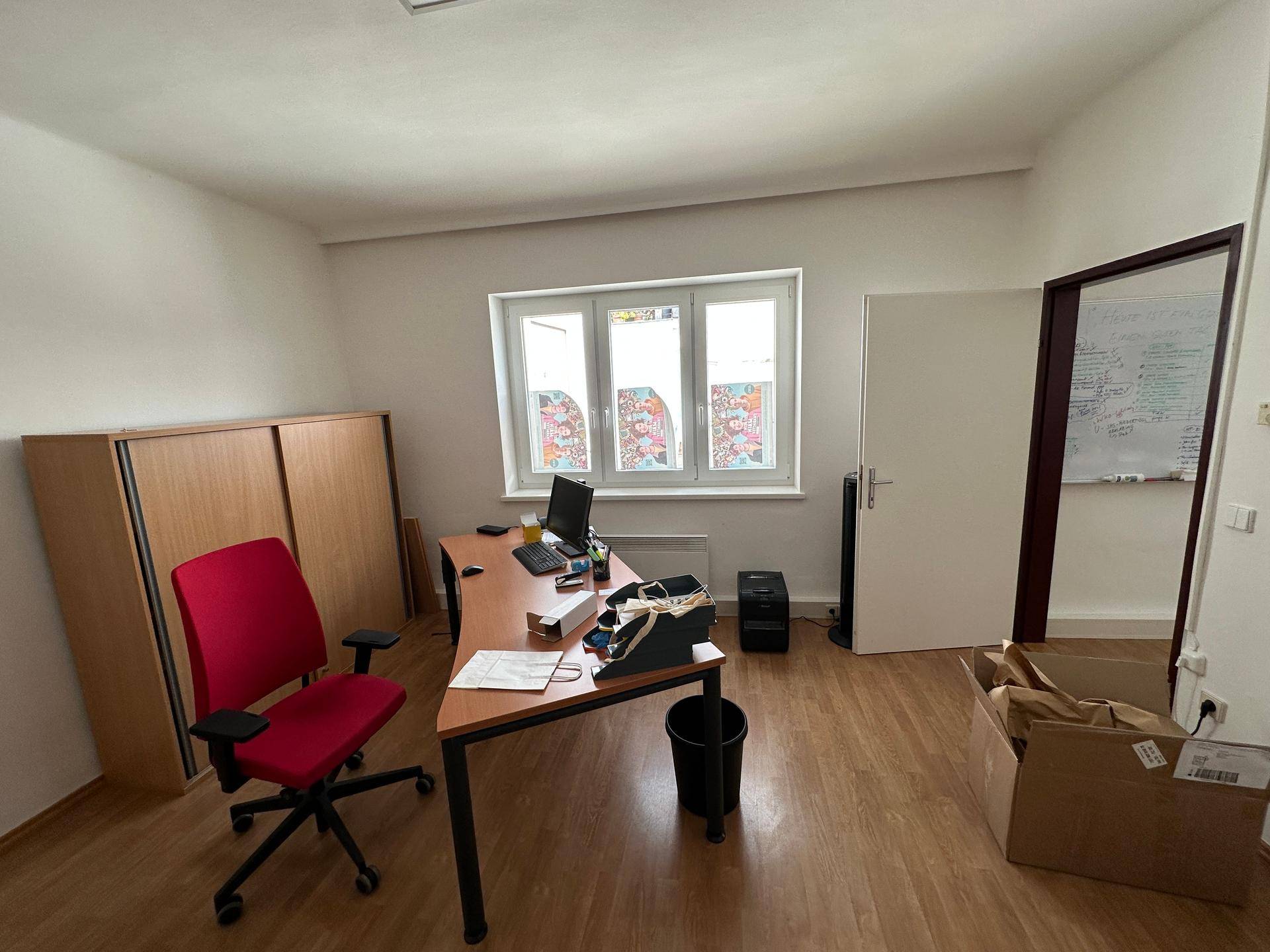 Modern eingerichtetes Büro mit Holzfußboden, großem Fenster und einem ergonomischen Schreibtischstuhl.
