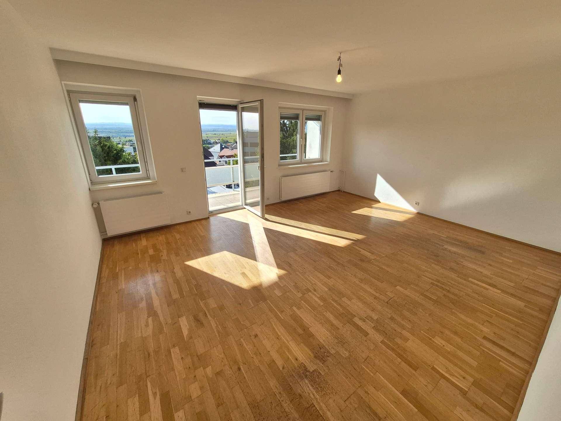 Helles Wohnzimmer mit Holzboden und Zugang zum Balkon, der viel Tageslicht hereinlässt.