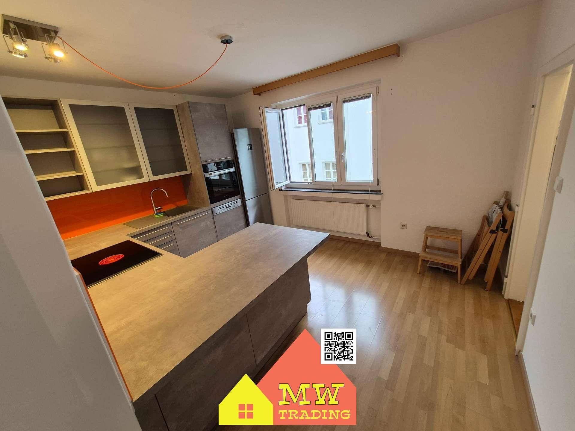 Moderne Küche mit grauen Schränken, orangefarbener Rückwand und integrierten Geräten sowie Holzboden.