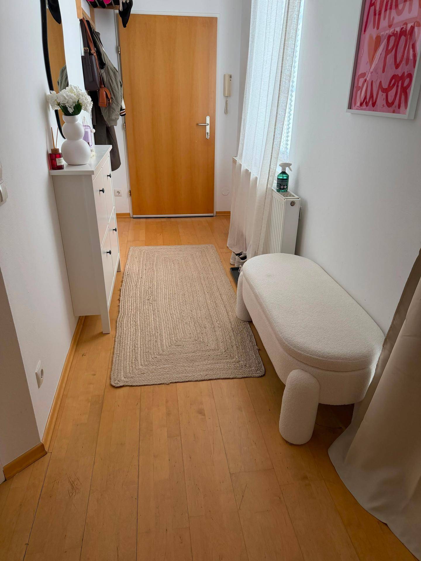 Heller Flur mit Holzboden, weißer Kommode und Garderobe.