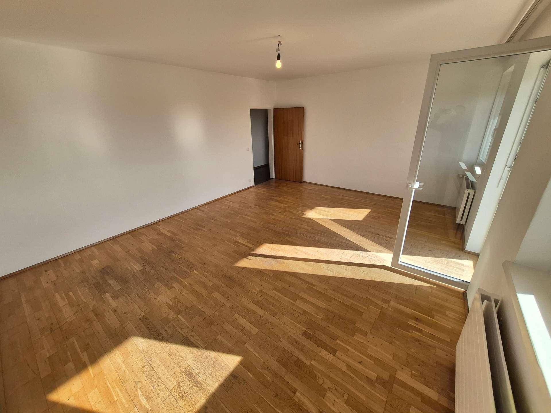 Geräumiges Wohnzimmer mit Holzboden und einem großen Fenster, das den Raum mit Licht füllt.