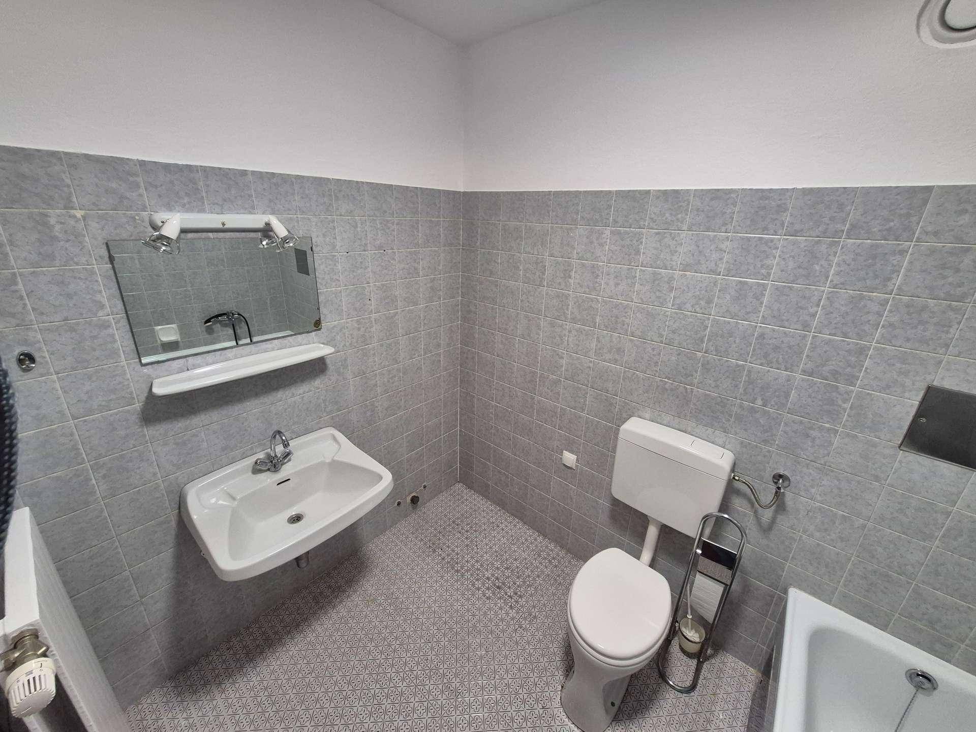 Badezimmer mit grauen Fliesen, Waschbecken, Spiegel und Toilette, funktional und sauber.