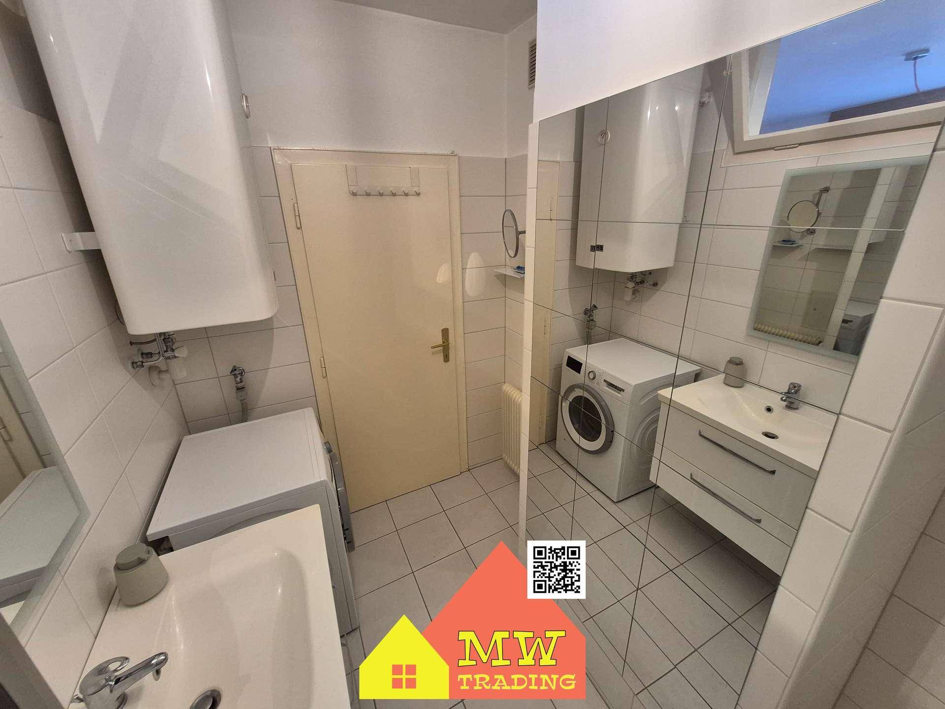 Funktionales Badezimmer mit Waschmaschine, Waschtisch und Boiler, alles in hellen Fliesen gehalten.