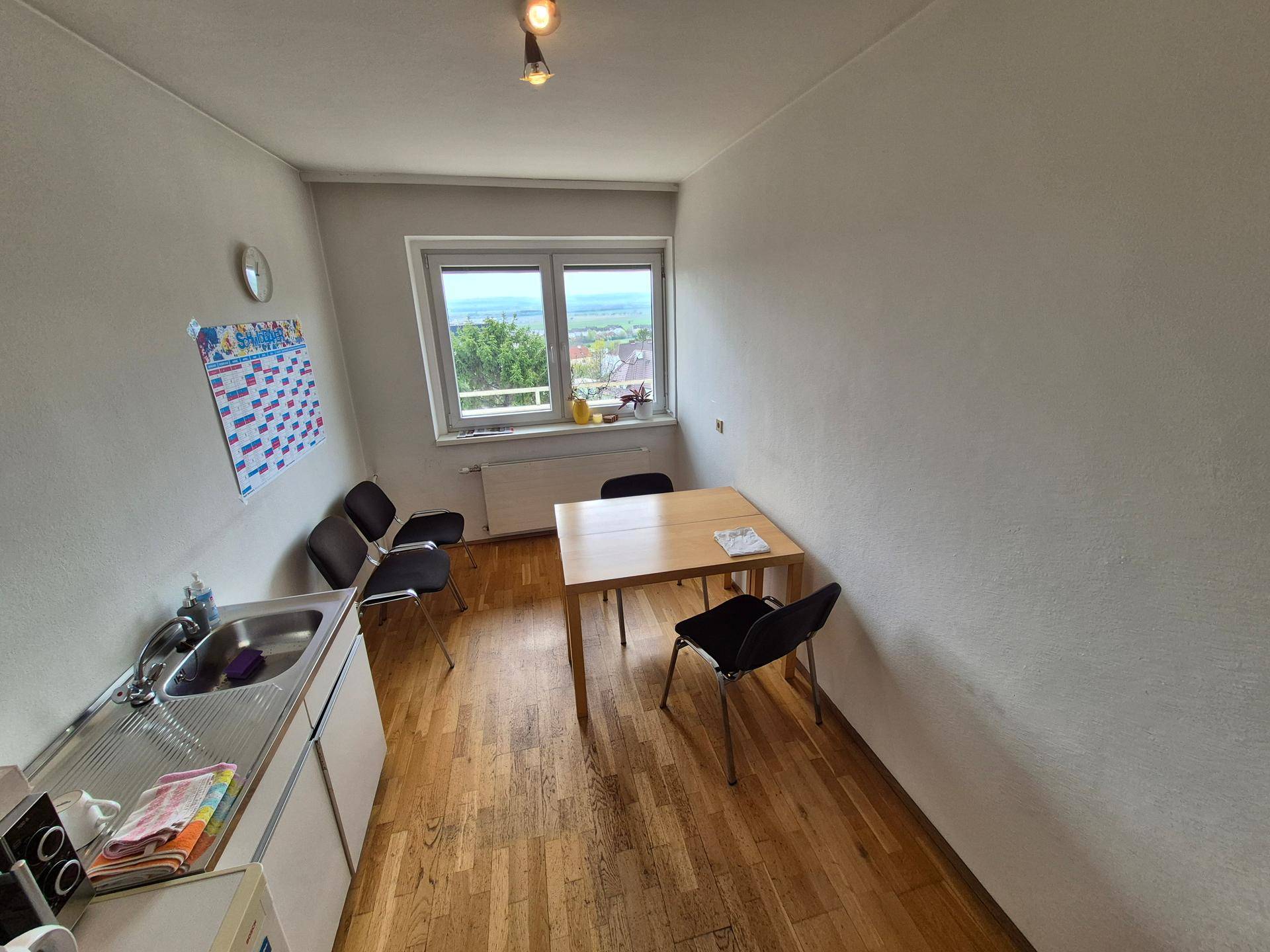 Einfache Teeküche mit Spüle, Kühlschrank und einem kleinen Esstisch mit Stühlen.