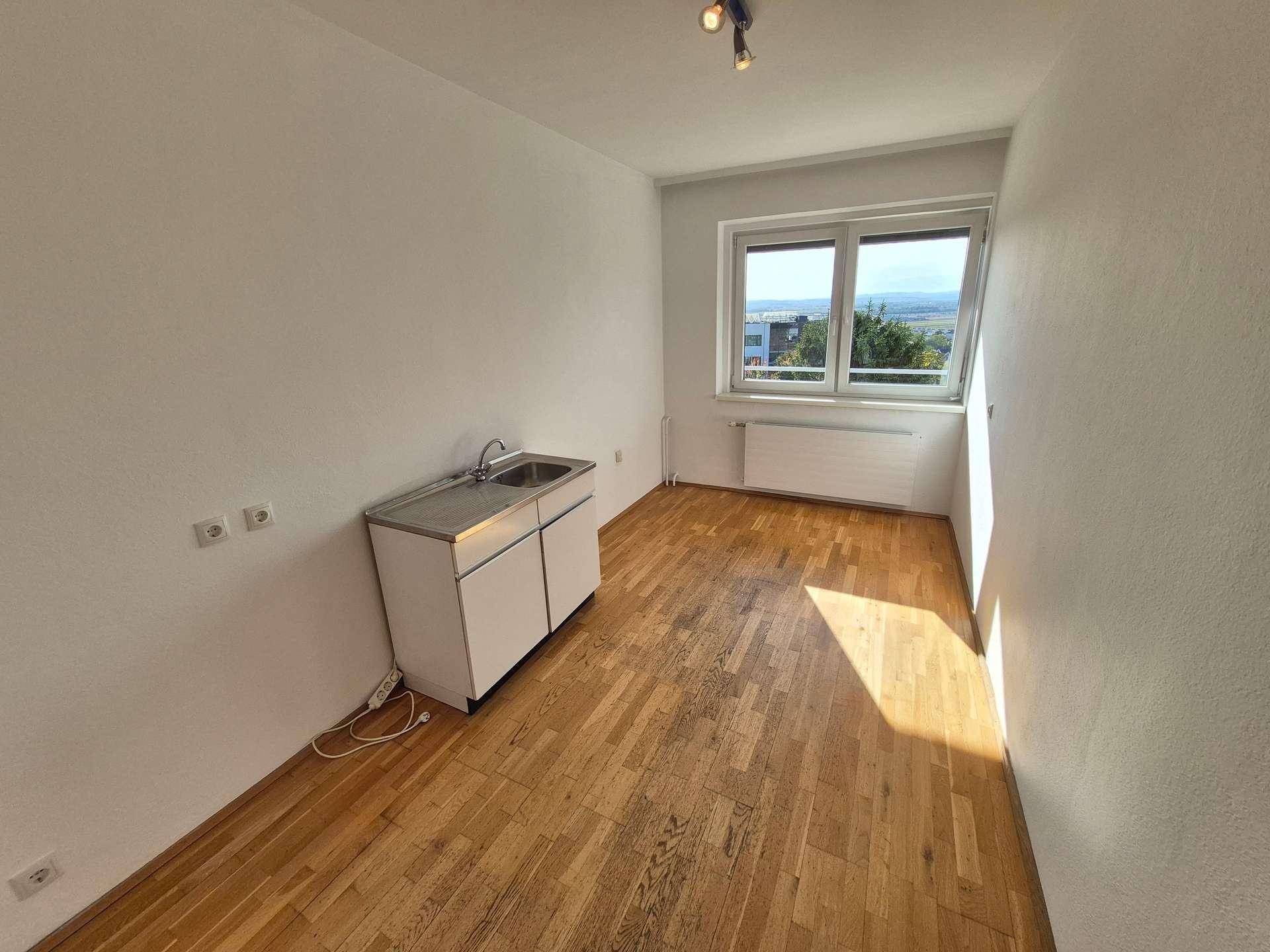 Heller Raum mit Holzboden und einer kleinen Küchenzeile, ideal für eine Kochnische.