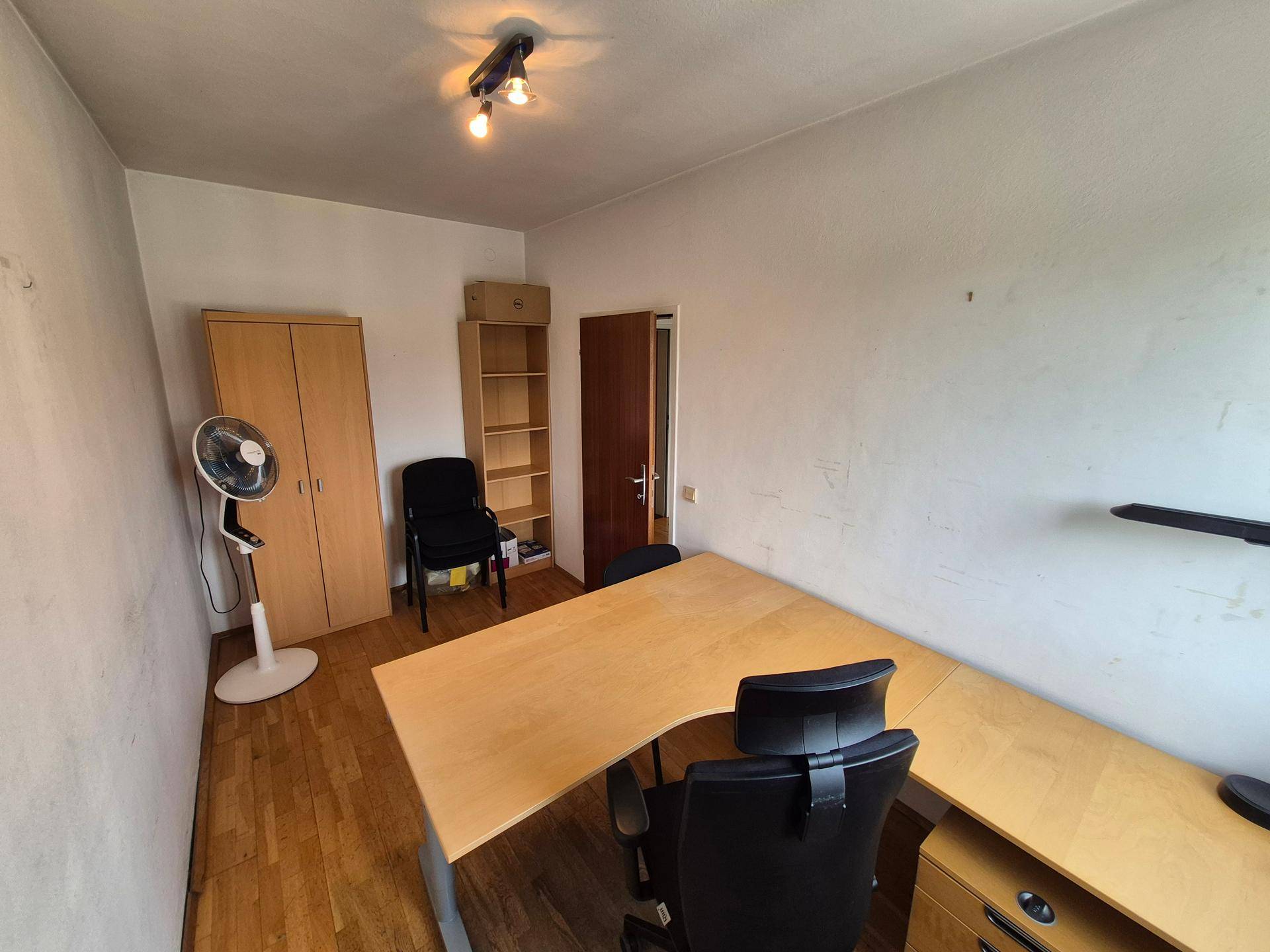 Büro mit Holzboden, Schreibtisch, Schrank und einem Ventilator für angenehme Kühlung.