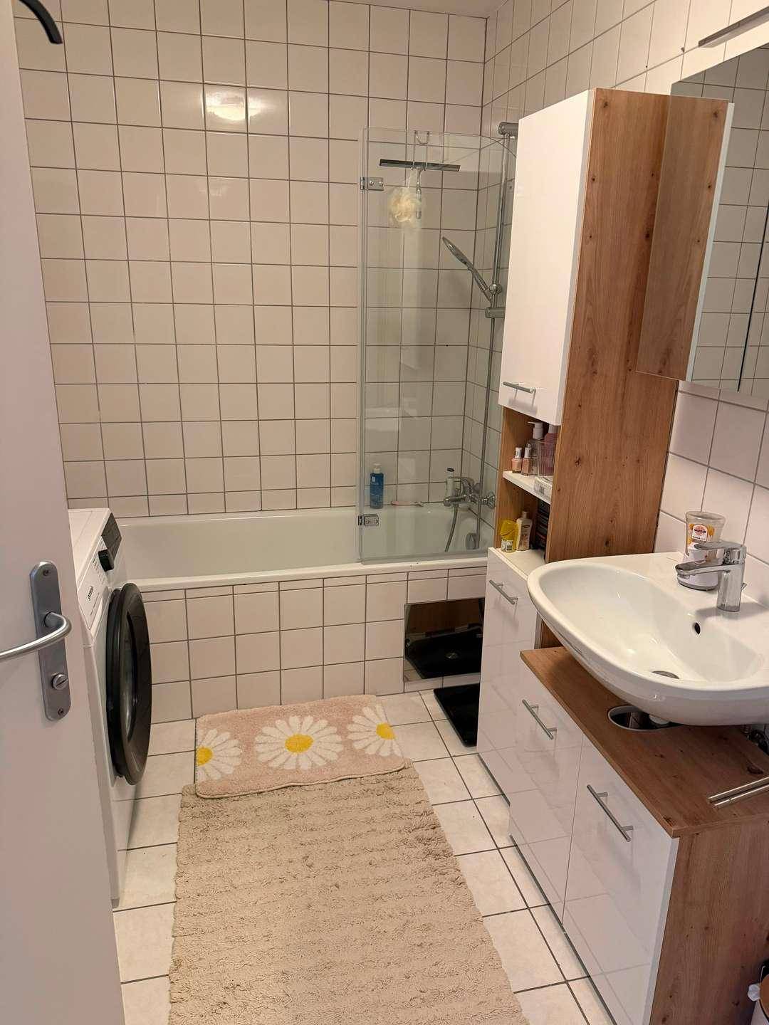Gefliestes Badezimmer mit Badewanne, Waschbecken und integrierter Waschmaschine.