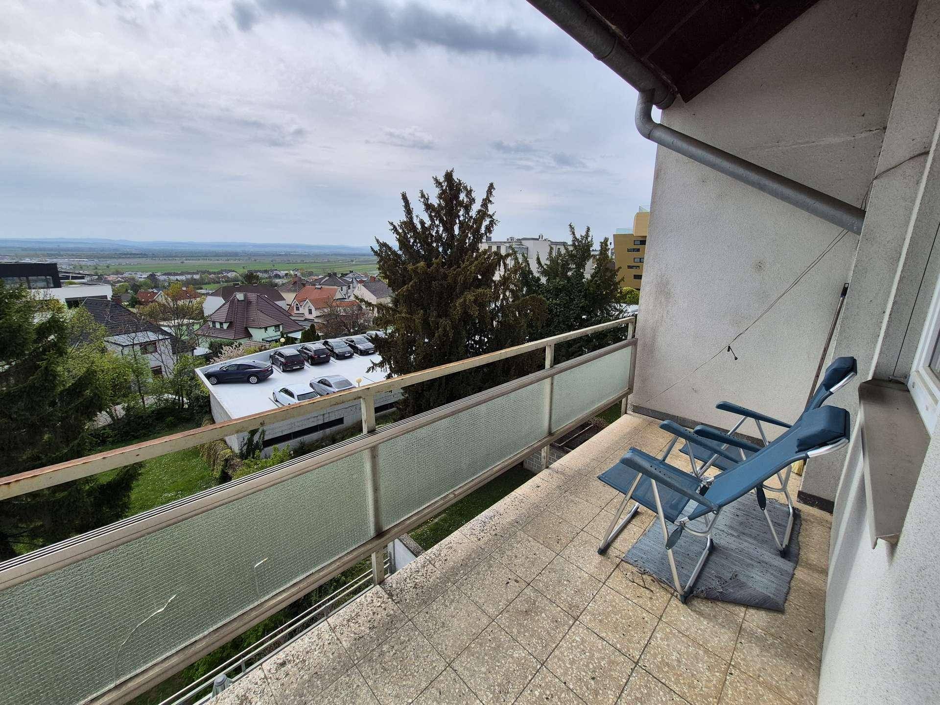 Geräumiger Balkon mit Fliesenboden und zwei Stühlen, bietet einen weiten Blick über die Stadt.