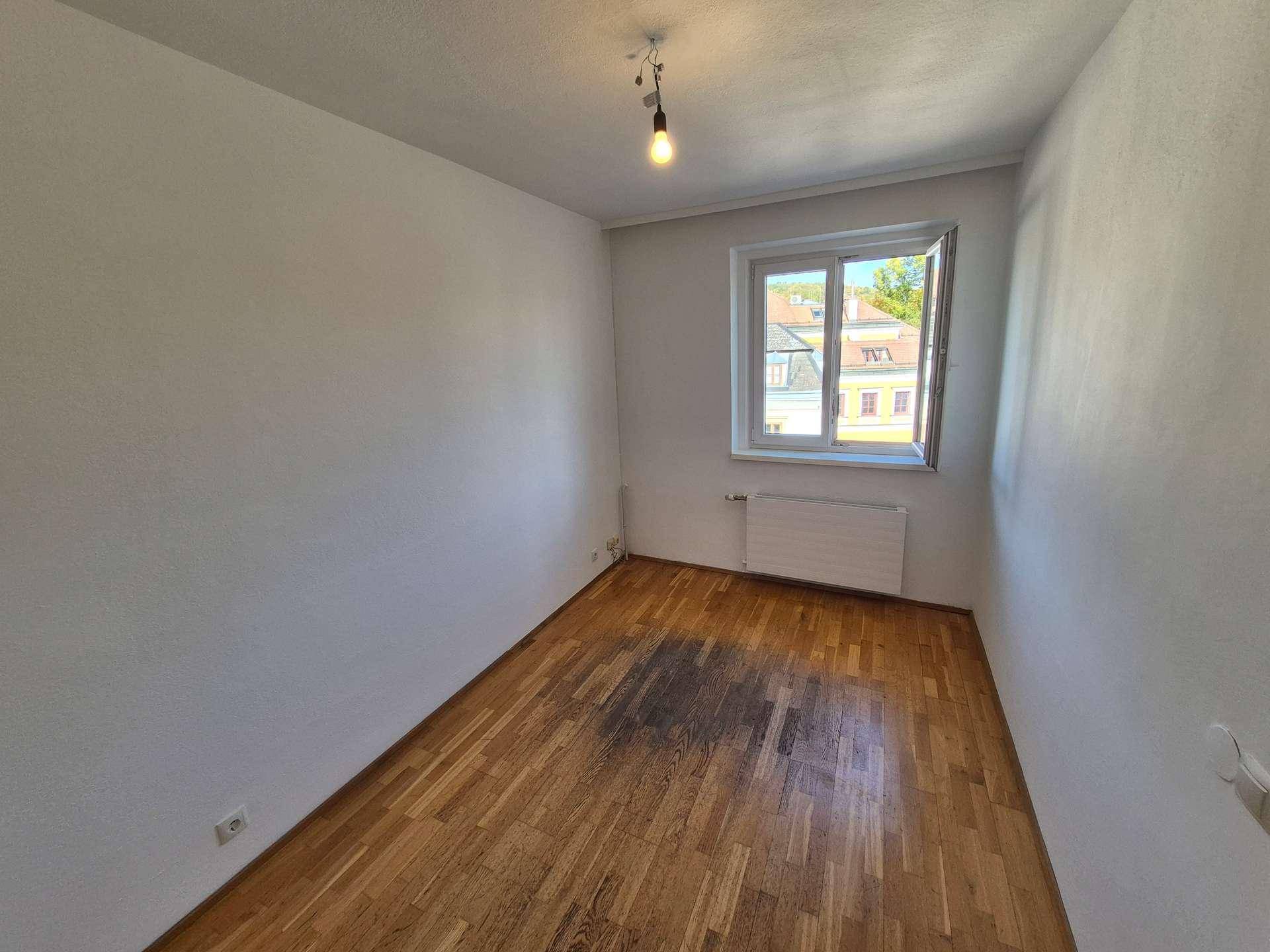Helles Schlafzimmer mit Holzboden und einem Fenster, das viel Tageslicht in den Raum bringt.
