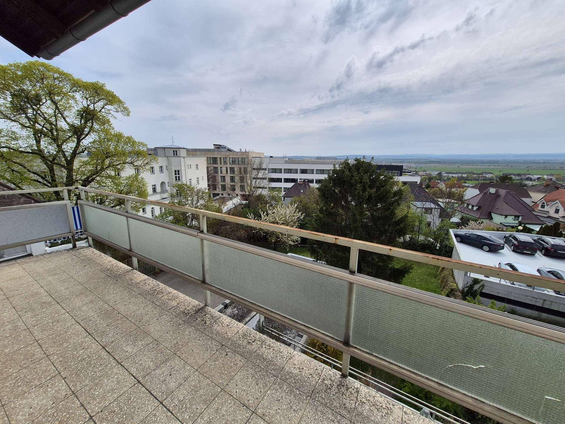 Heller Balkon mit Fliesenboden und Blick auf umliegende Gebäude, Bäume und die weite Landschaft.
