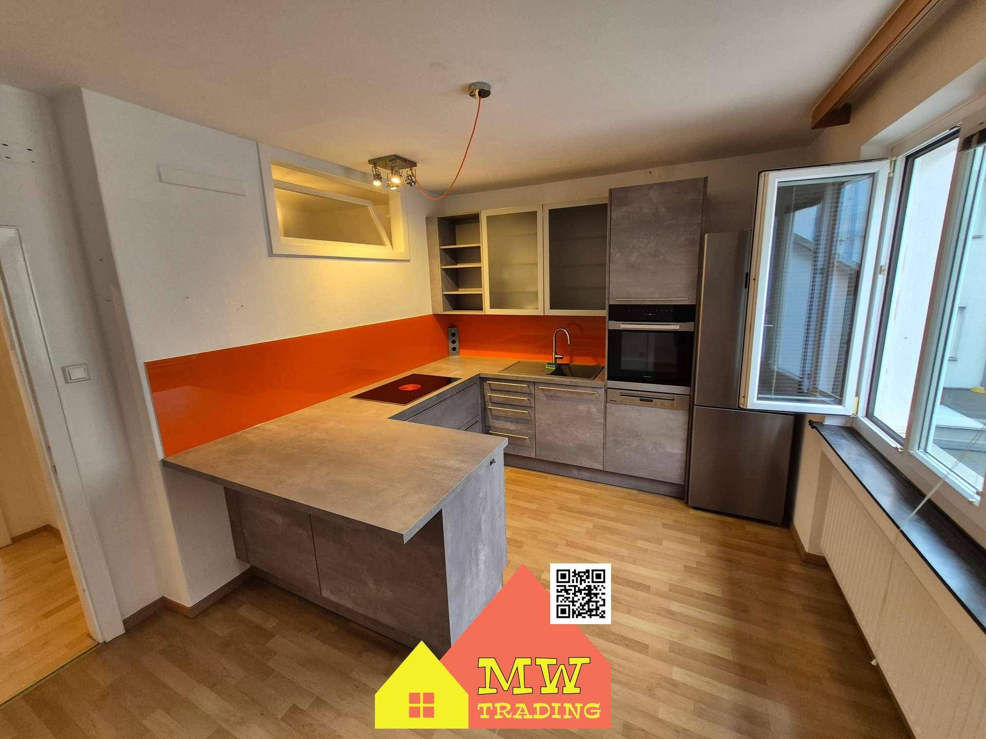 Moderne Küche mit grauen Schränken, orangefarbener Rückwand und integrierten Geräten sowie Holzboden.