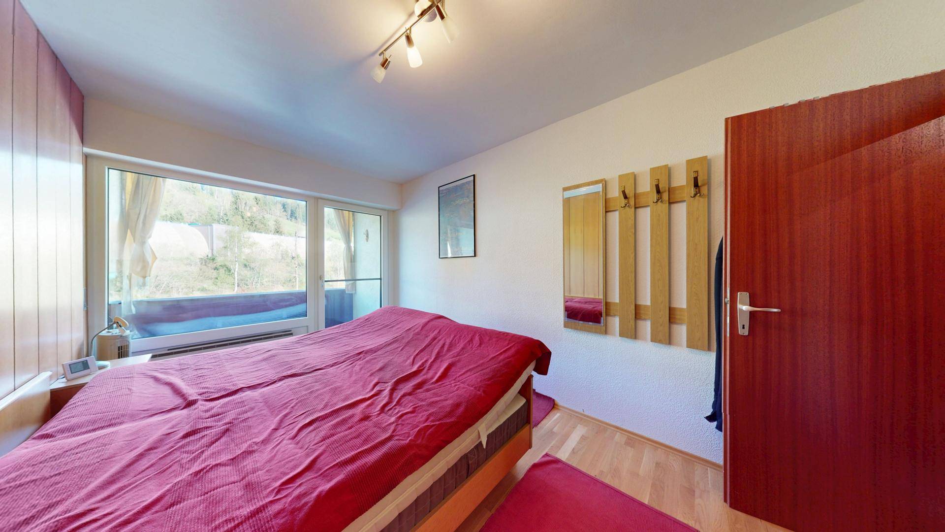 Helles Schlafzimmer mit Holzboden, Doppelbett und einem Kleiderhaken an der Wand.
