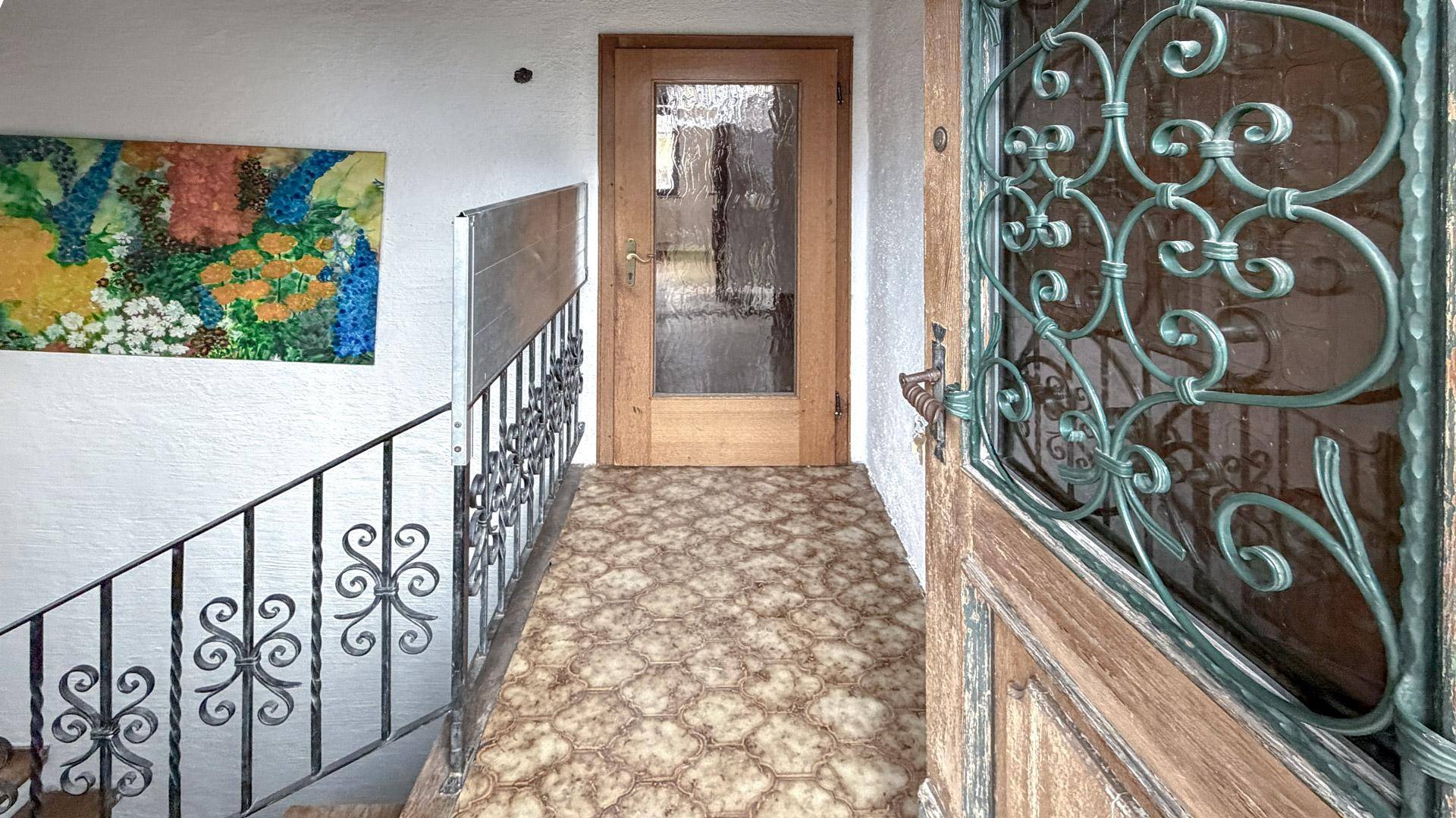 Eingangsbereich mit gemustertem Boden, schmiedeeisernem Geländer und Holztreppe.