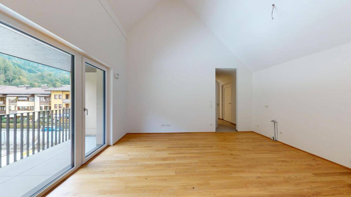 Heller Wohnbereich mit Holzboden und großen Schiebetüren, die auf einen Balkon führen.