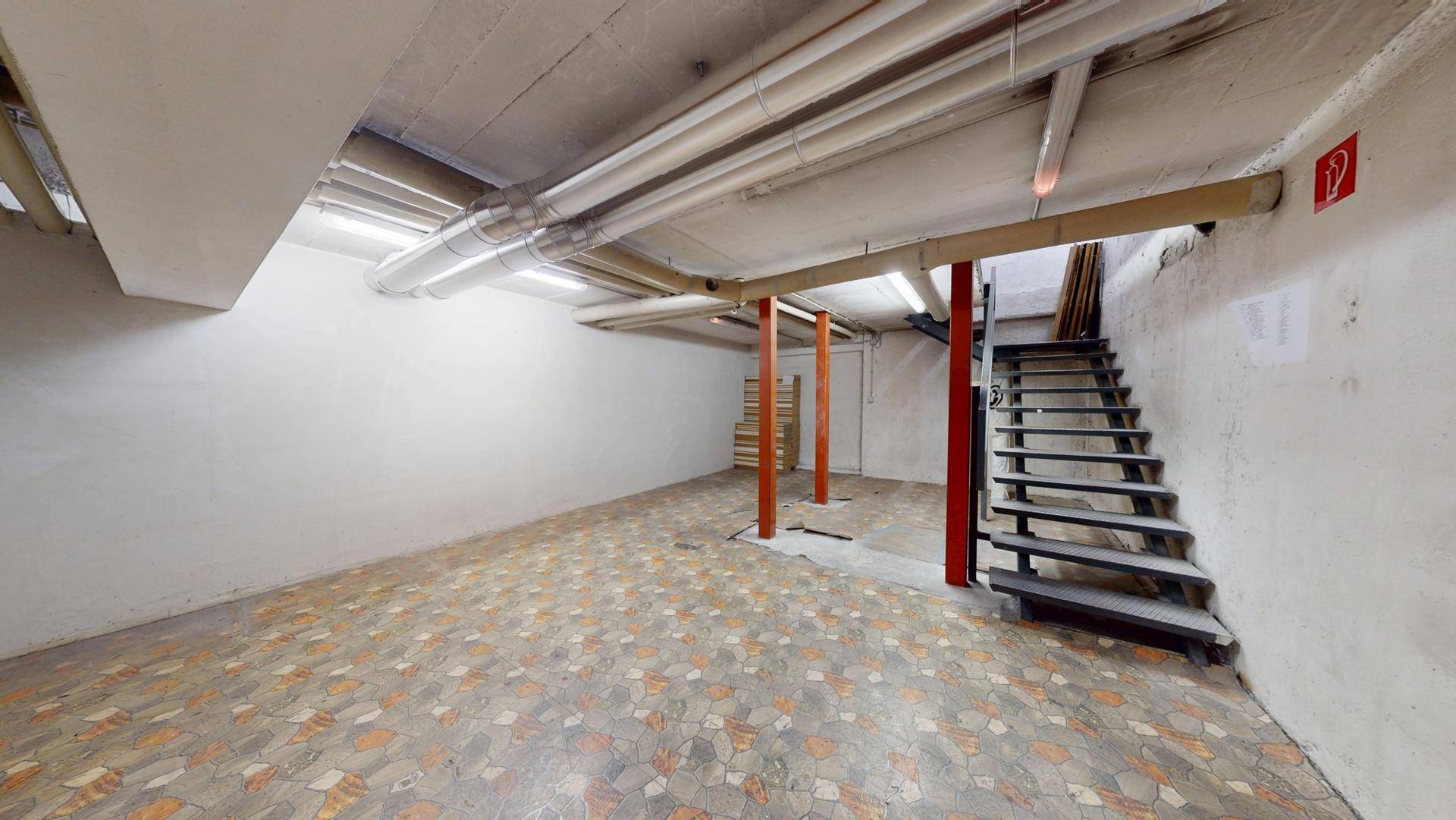 Geräumiger Kellerraum mit Fliesenboden, sichtbaren Rohren und einer Metalltreppe.