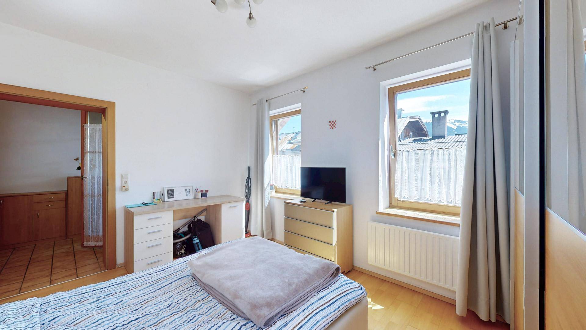 Schlafzimmer mit Schreibtisch, Kommode und Blick aus dem Fenster auf die Umgebung.