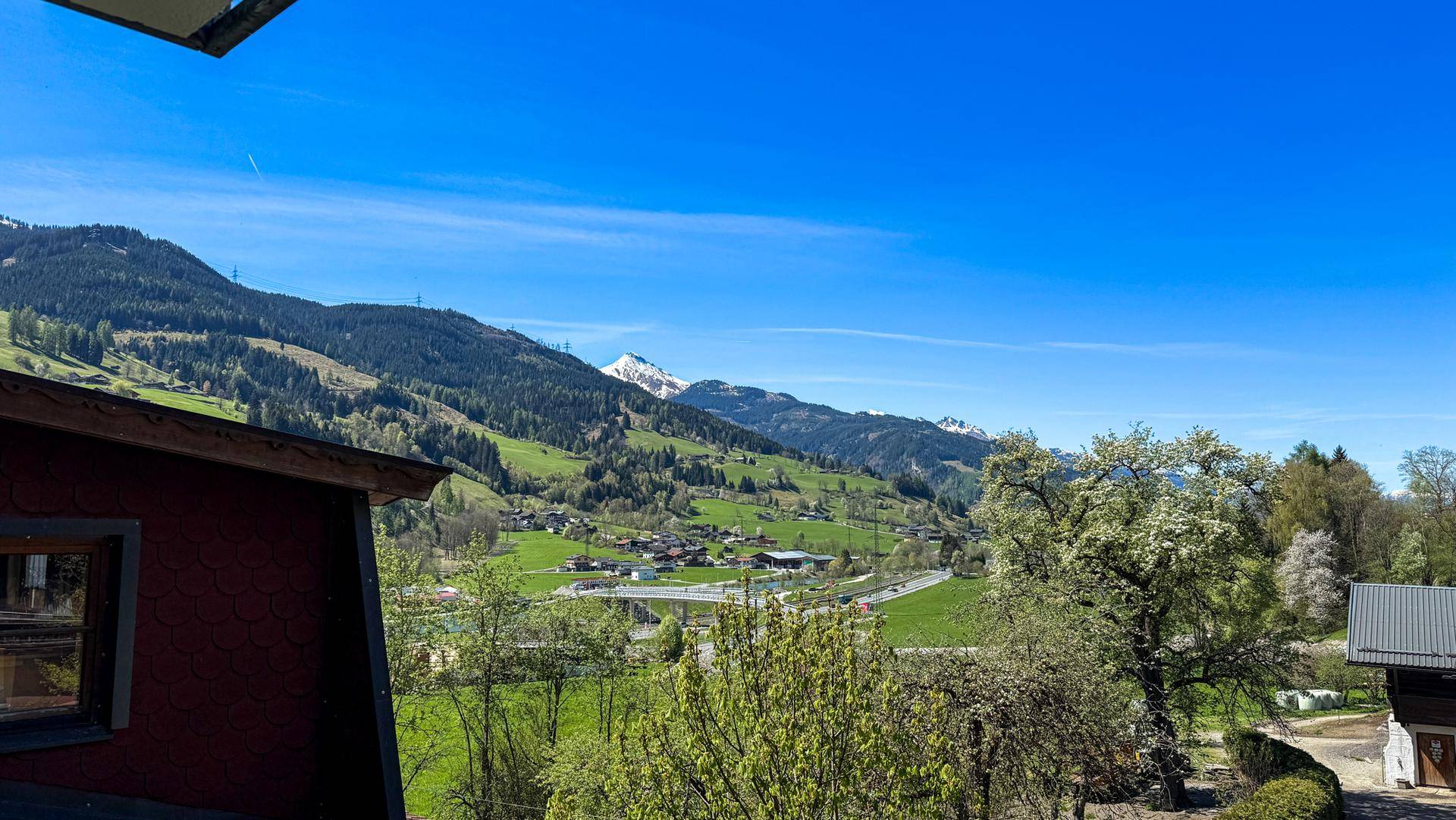 Malerischer Ausblick auf die grüne Berglandschaft mit schneebedeckten Gipfeln und Dörfern.