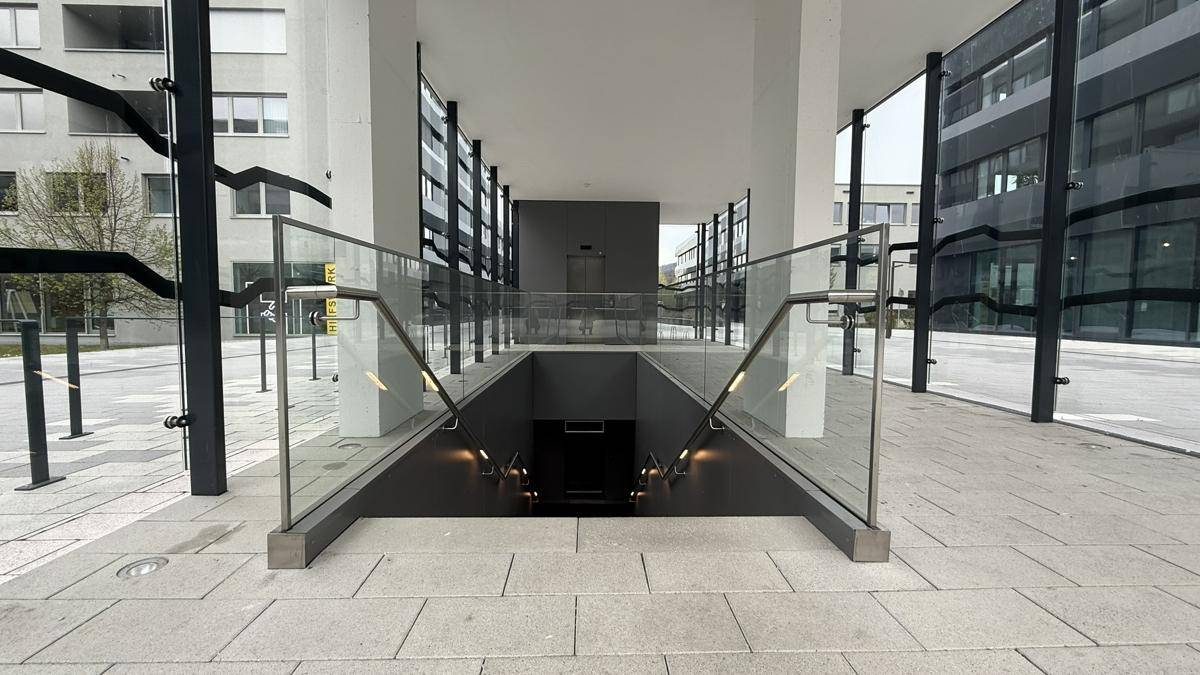 Eingang zu einer Tiefgarage oder einem Kellerbereich mit moderner Glasbrüstung und Treppe.
