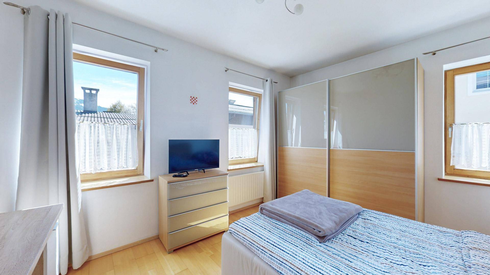 Geräumiges Schlafzimmer mit großem Schiebetürenschrank, Kommode und hellen Vorhängen.