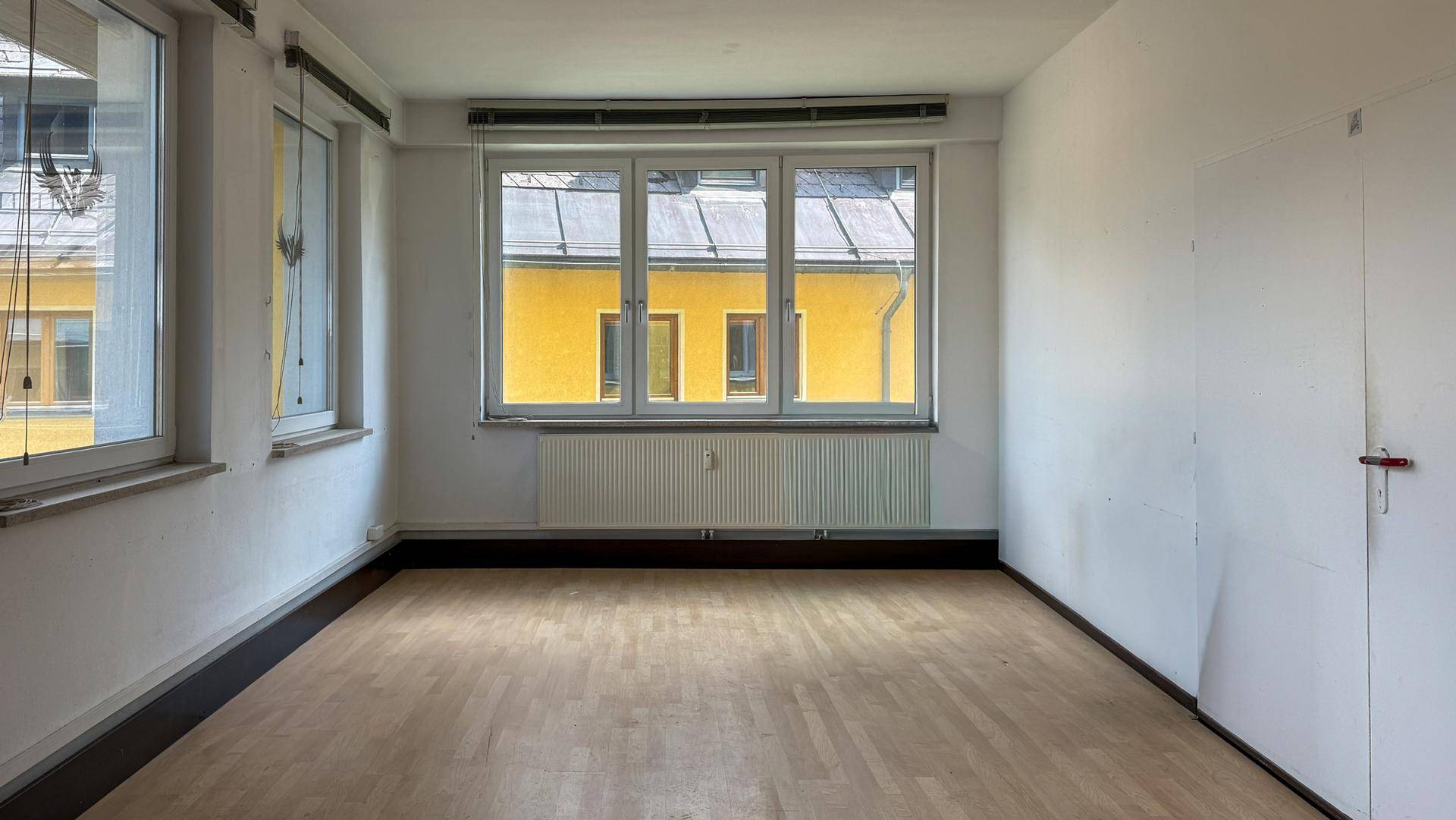 Heller, leerer Büroraum mit großen Fenstern und Holzboden, bereit zur individuellen Gestaltung.