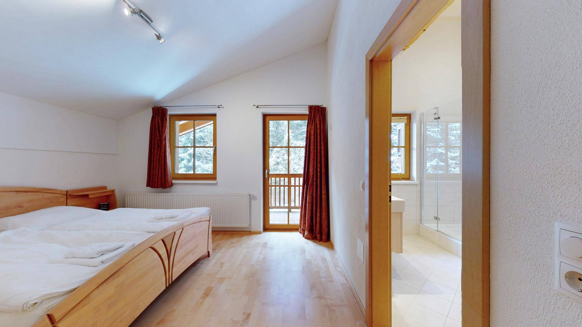 Schlafzimmer mit Holzbett und direktem Zugang zu einem modernen Badezimmer.