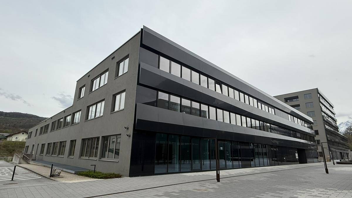 Modernes Bürogebäude mit dunkler Fassade und großen Fenstern, umgeben von einer gepflegten Außenanlage.