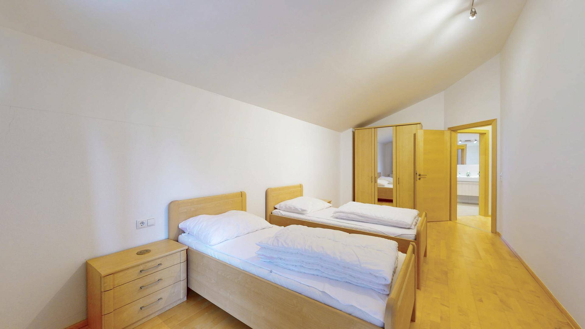 Schlafzimmer mit zwei Einzelbetten, Holzmöbeln und Dachschräge.