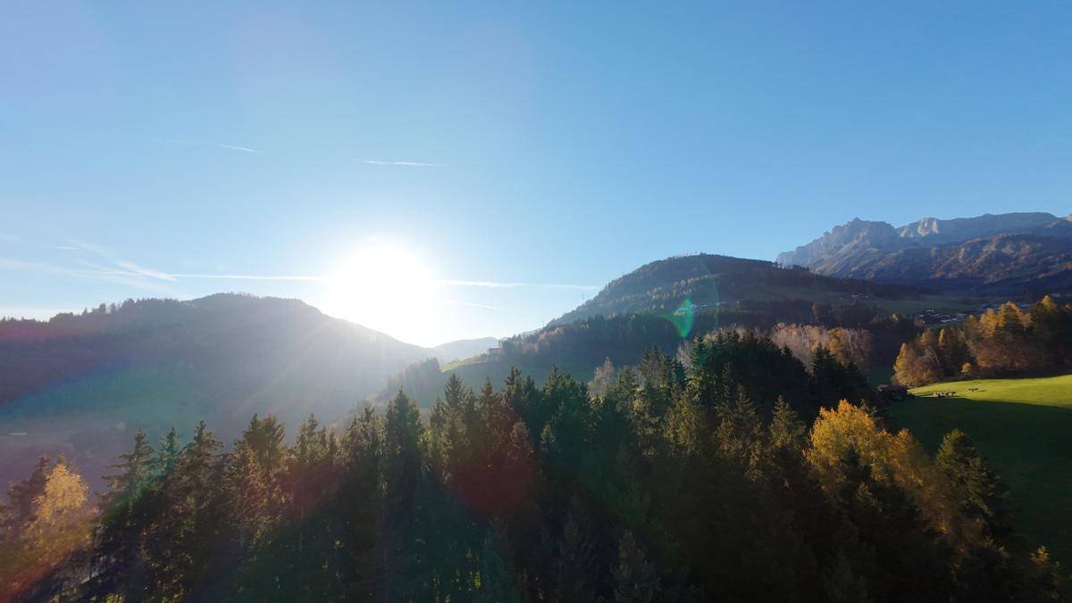 Sonnenaufgang über bewaldeten Hügeln und Bergen, mit hellem Licht am Horizont.
