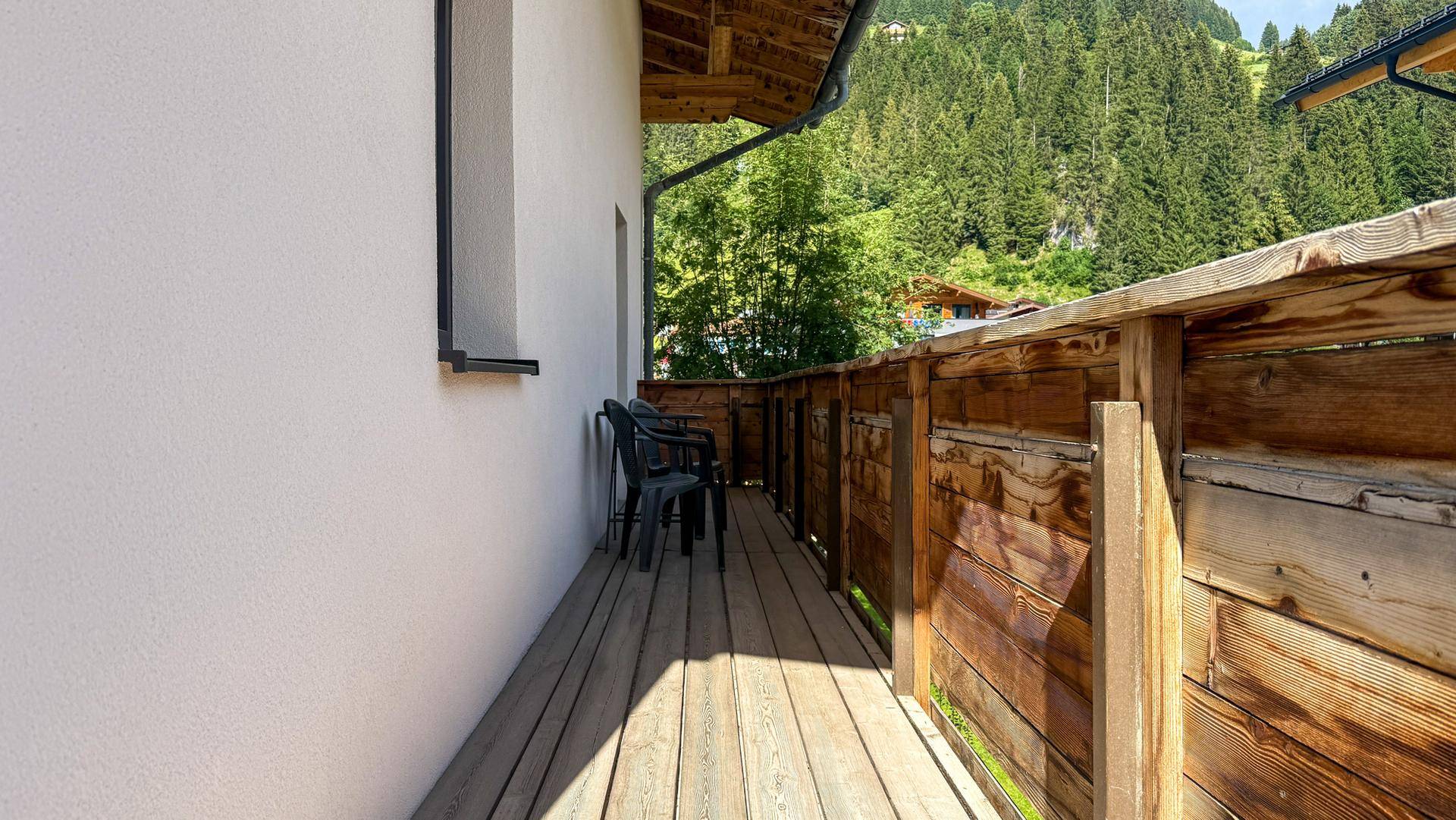 Langer Balkon mit Holzboden und Blick auf die bewaldeten Hänge.