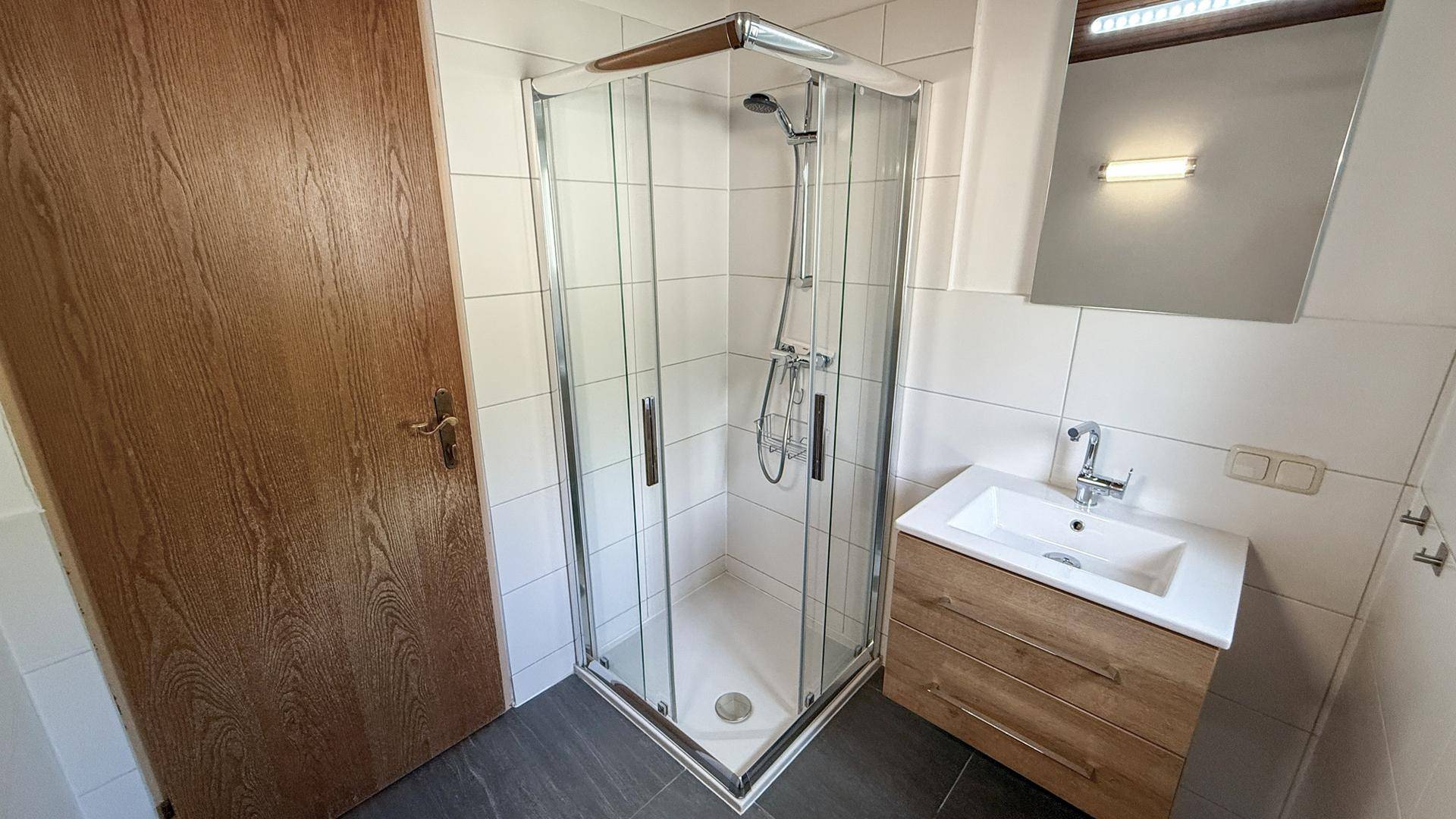 Modernes Badezimmer mit Duschkabine, Waschbecken und hellen Fliesen.