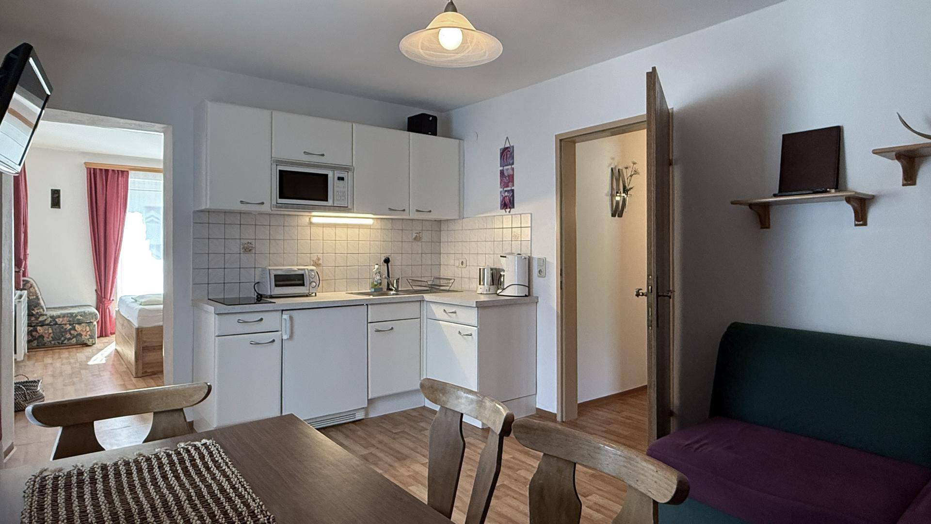 Funktionale Küche mit weißen Schränken, Fliesenrückwand und Blick in den Schlafbereich.