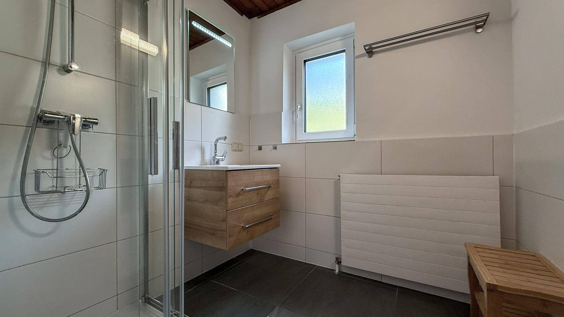 Badezimmer mit Duschkabine, Waschbecken, Fenster und Handtuchhalter.