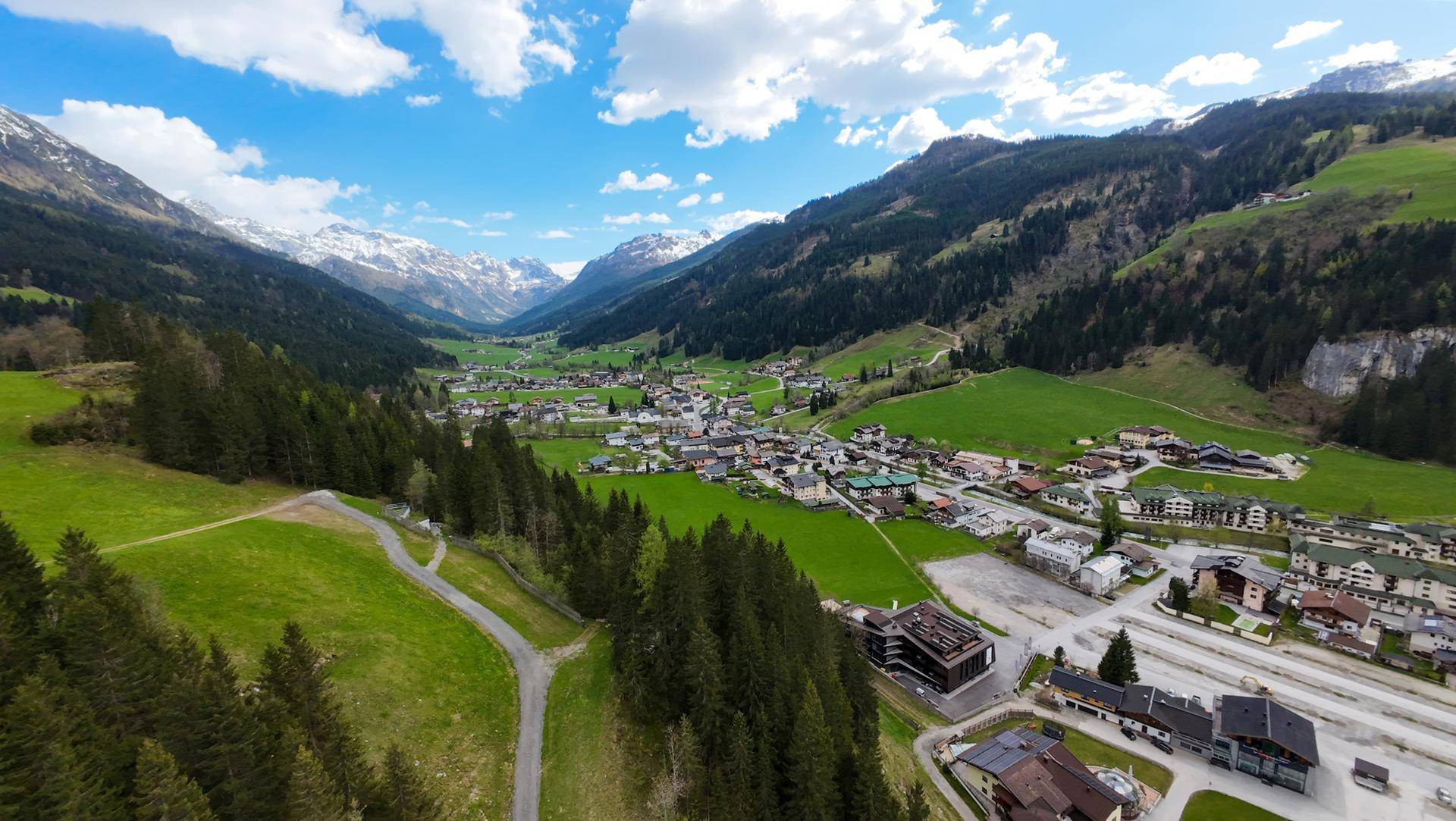 Malerisches Dorf in einem grünen Tal, umgeben von Bergen unter blauem Himmel.
