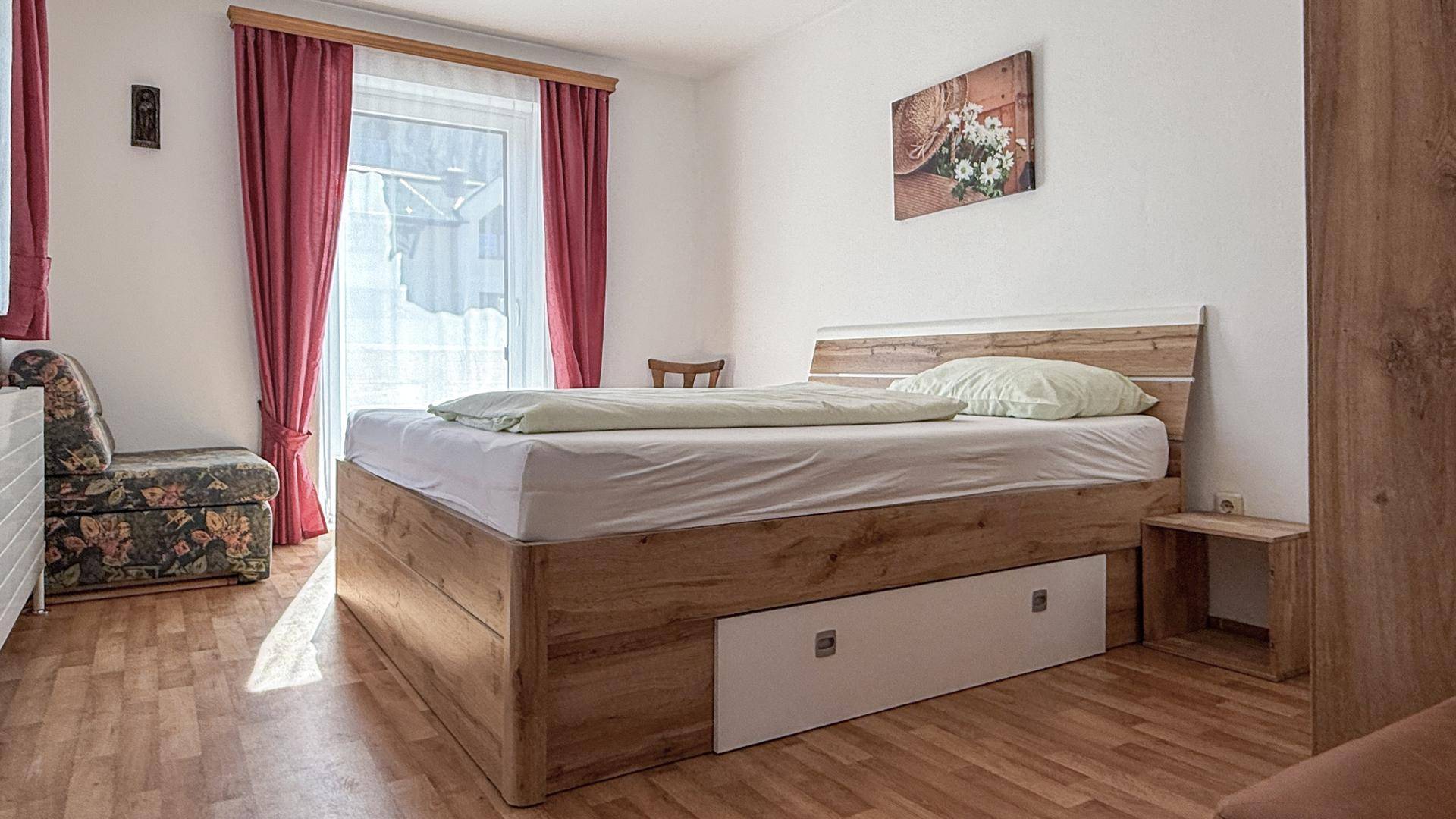 Helles Schlafzimmer mit Doppelbett, Holzrahmen und Zugang zum Balkon.
