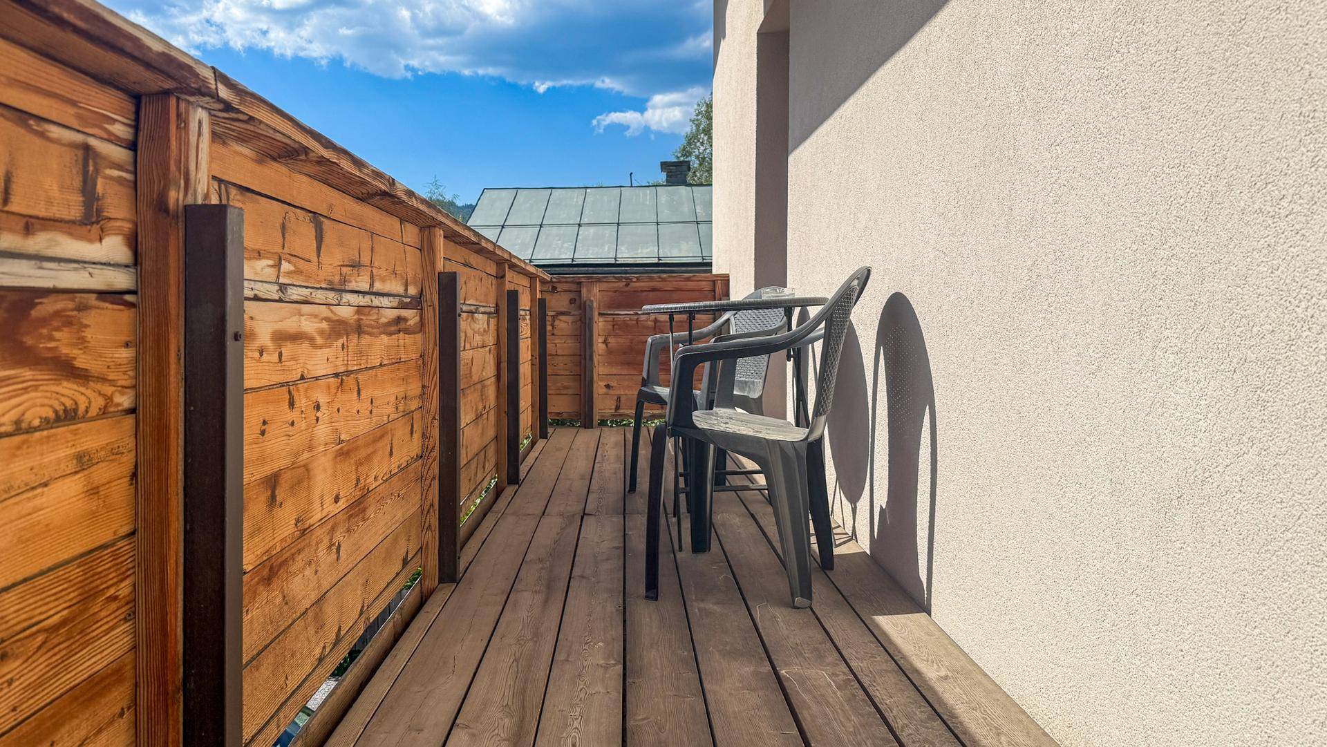 Sonniger Balkon mit Holzboden und Sitzgelegenheiten, umgeben von einer Holzverkleidung.