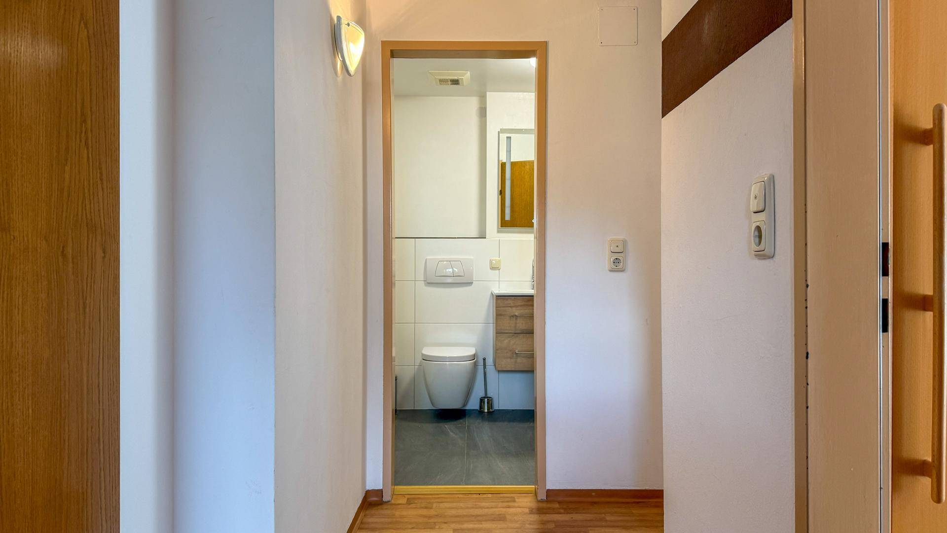 Heller Flur mit Holzboden, der zum modernen Badezimmer führt.