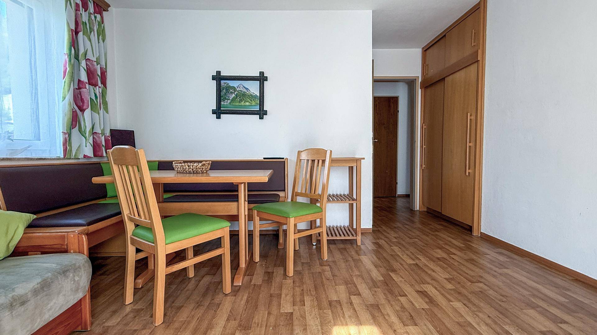 Wohn- und Essbereich mit Holzboden, integrierter Eckbank und Zugang zu weiteren Räumen.